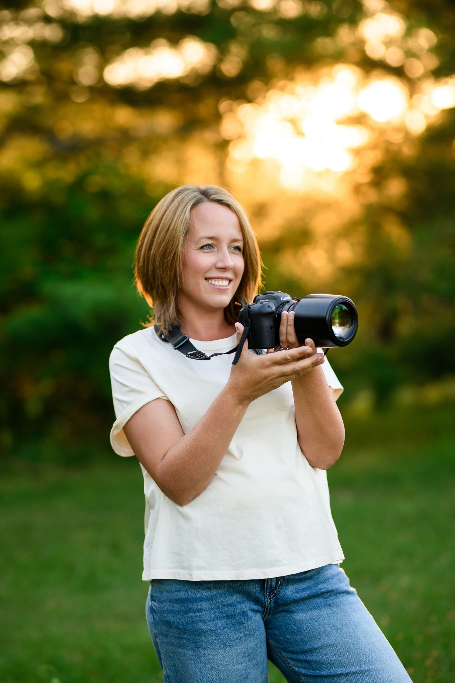 A photographer smiling while holding a professional camera at sunset in a garden.