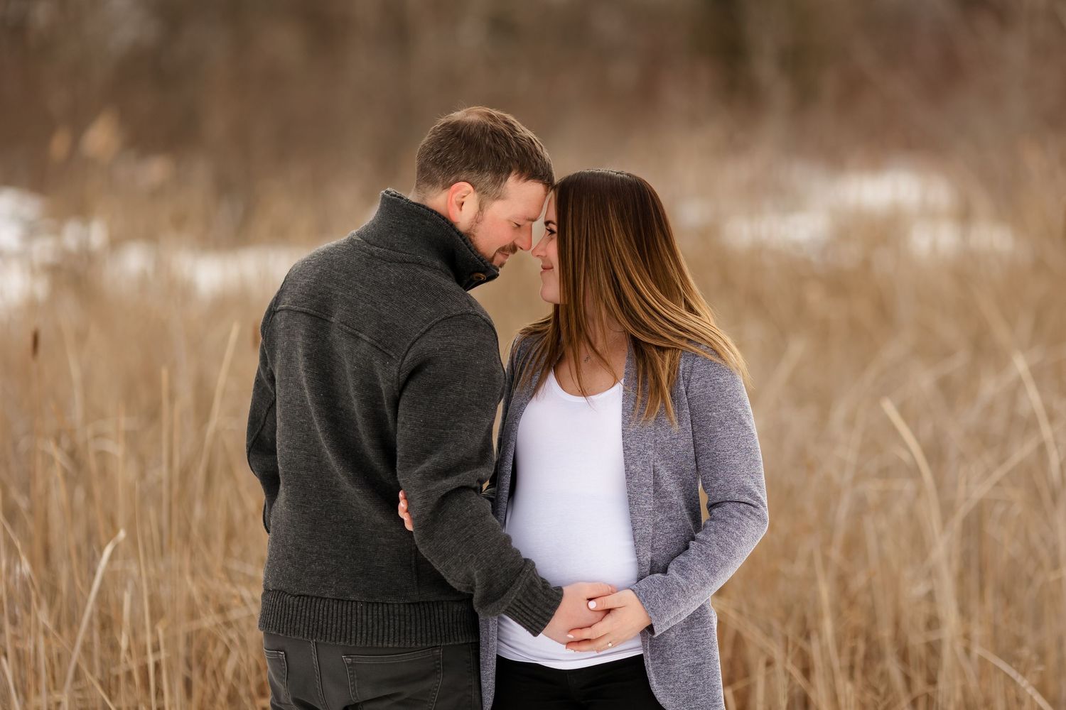 Intimate winter maternity moment with couple in snow covered field.
