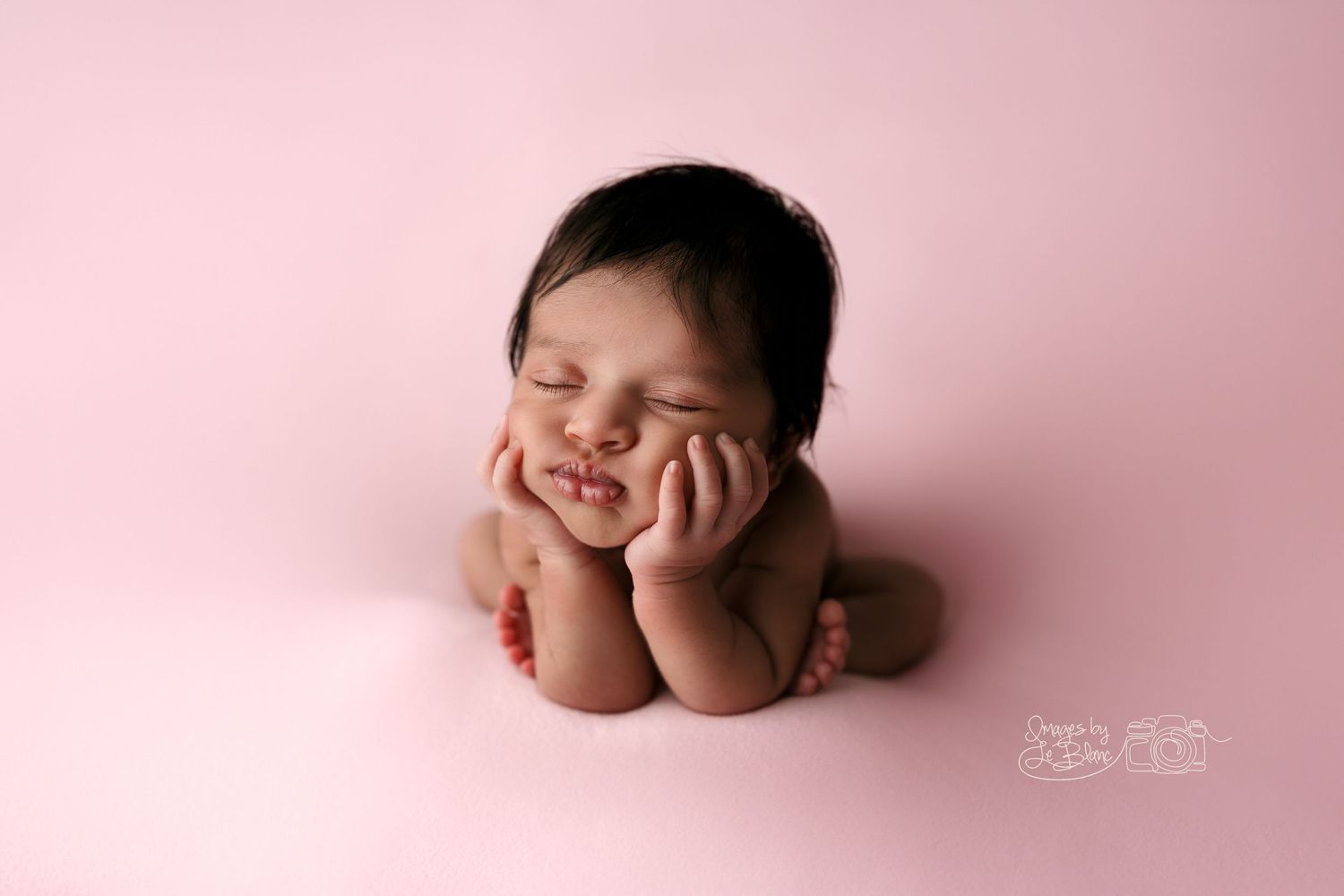 Adorable newborn photo with hands under chin on pink background.