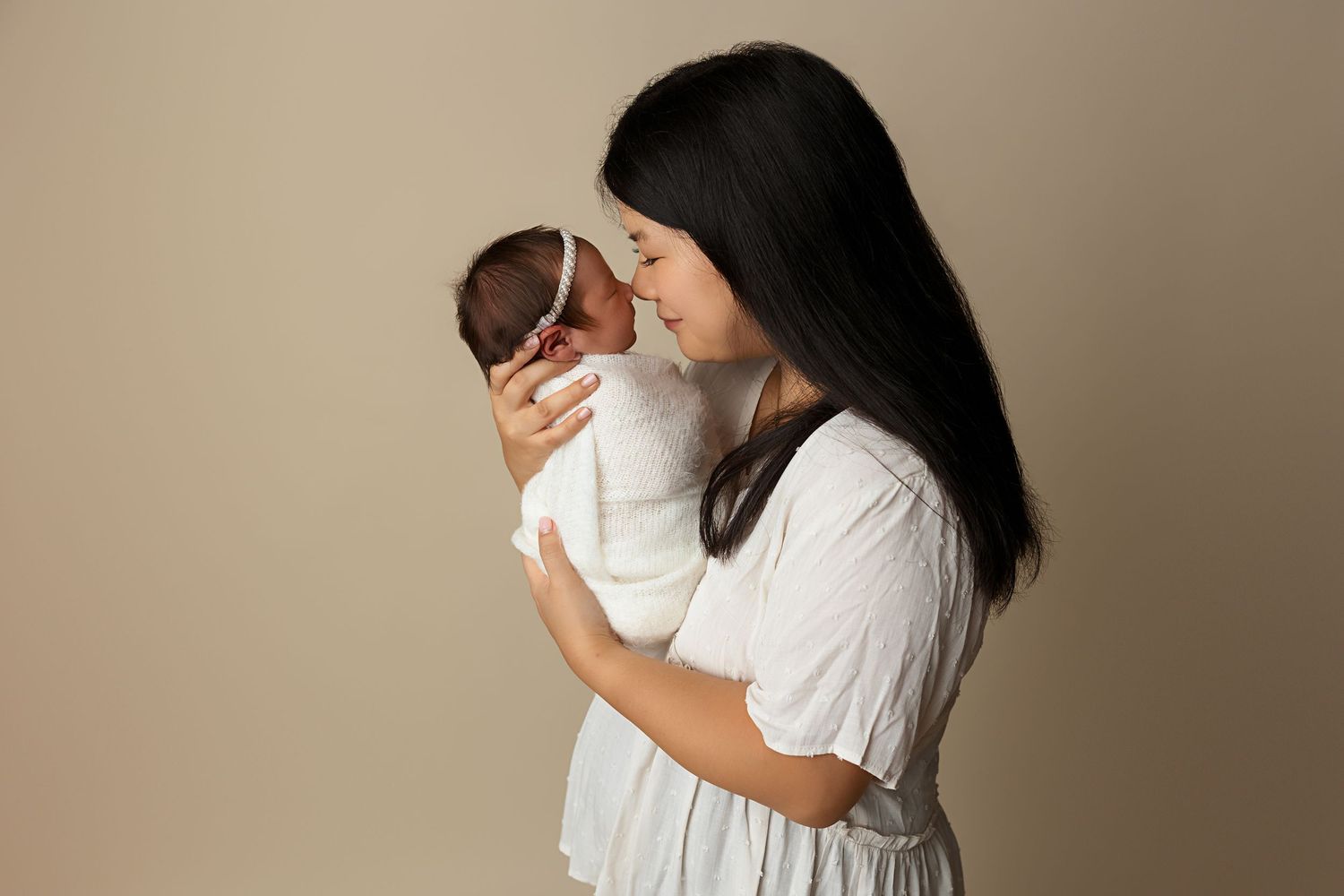 A loving newborn photography moment captured against a neutral backdrop.