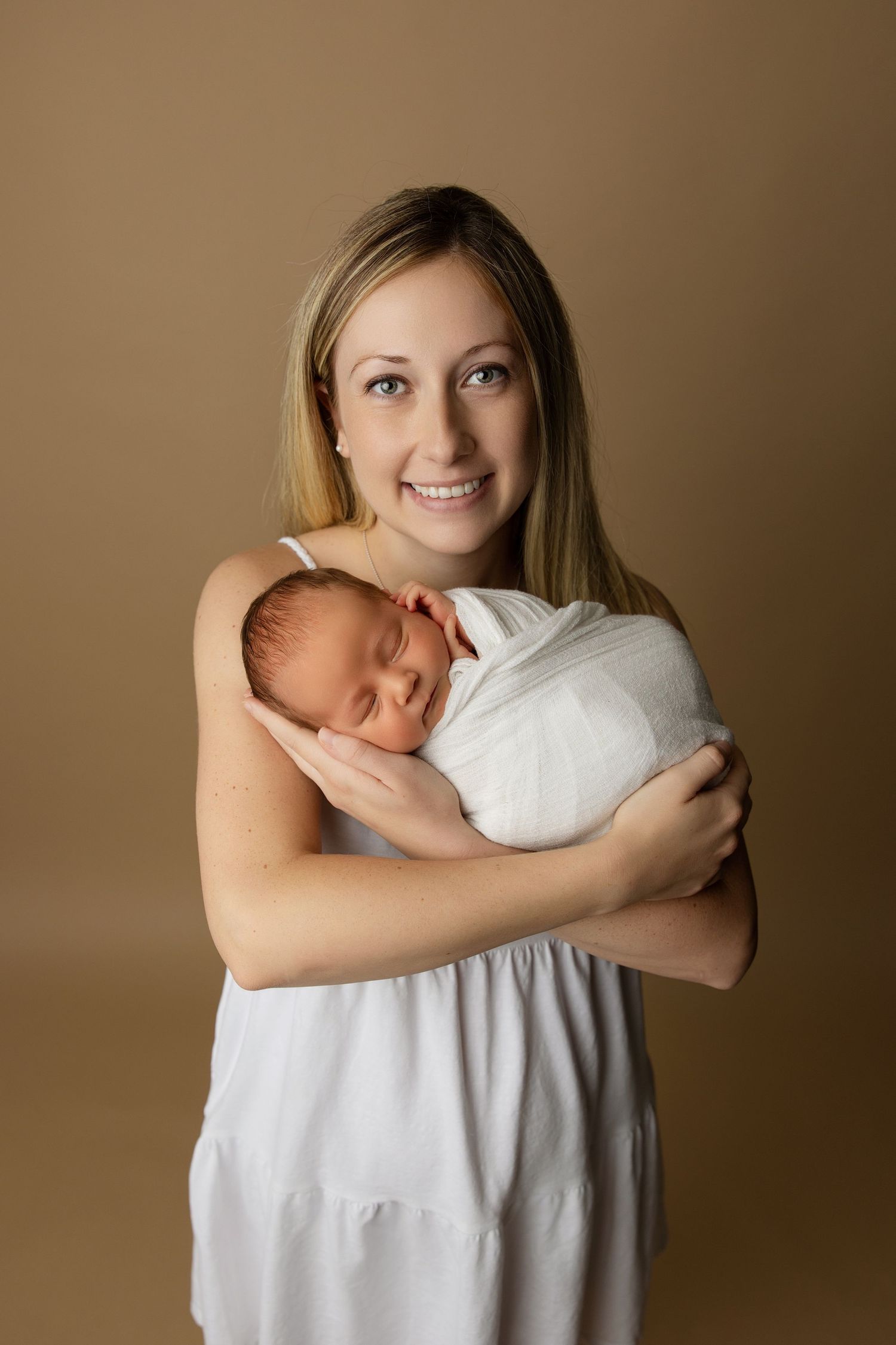 Intimate family portrait with newborn against warm brown background.