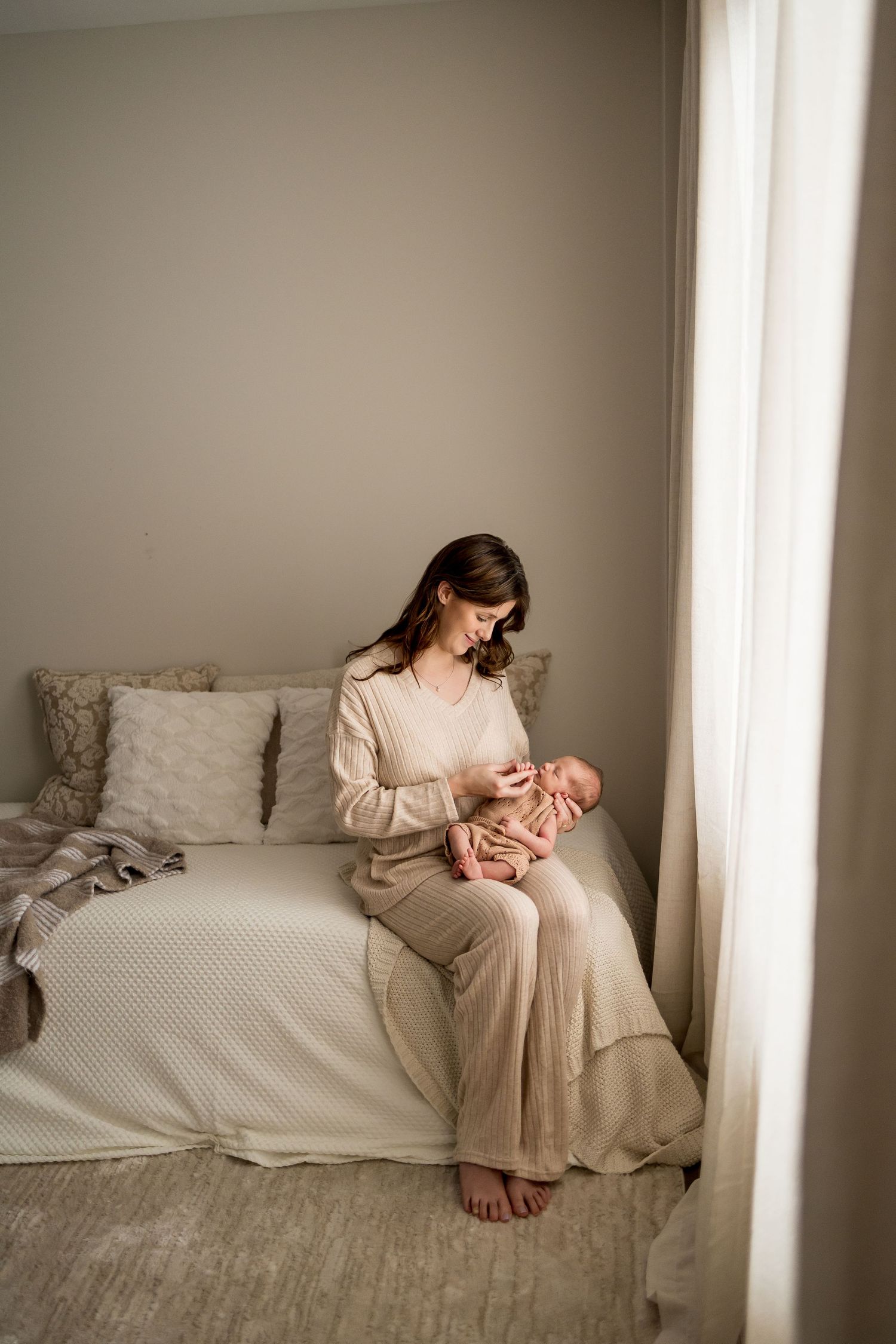 A series of four intimate photos showing tender moments between mother and newborn in a soft, neutral-toned bedroom setting.