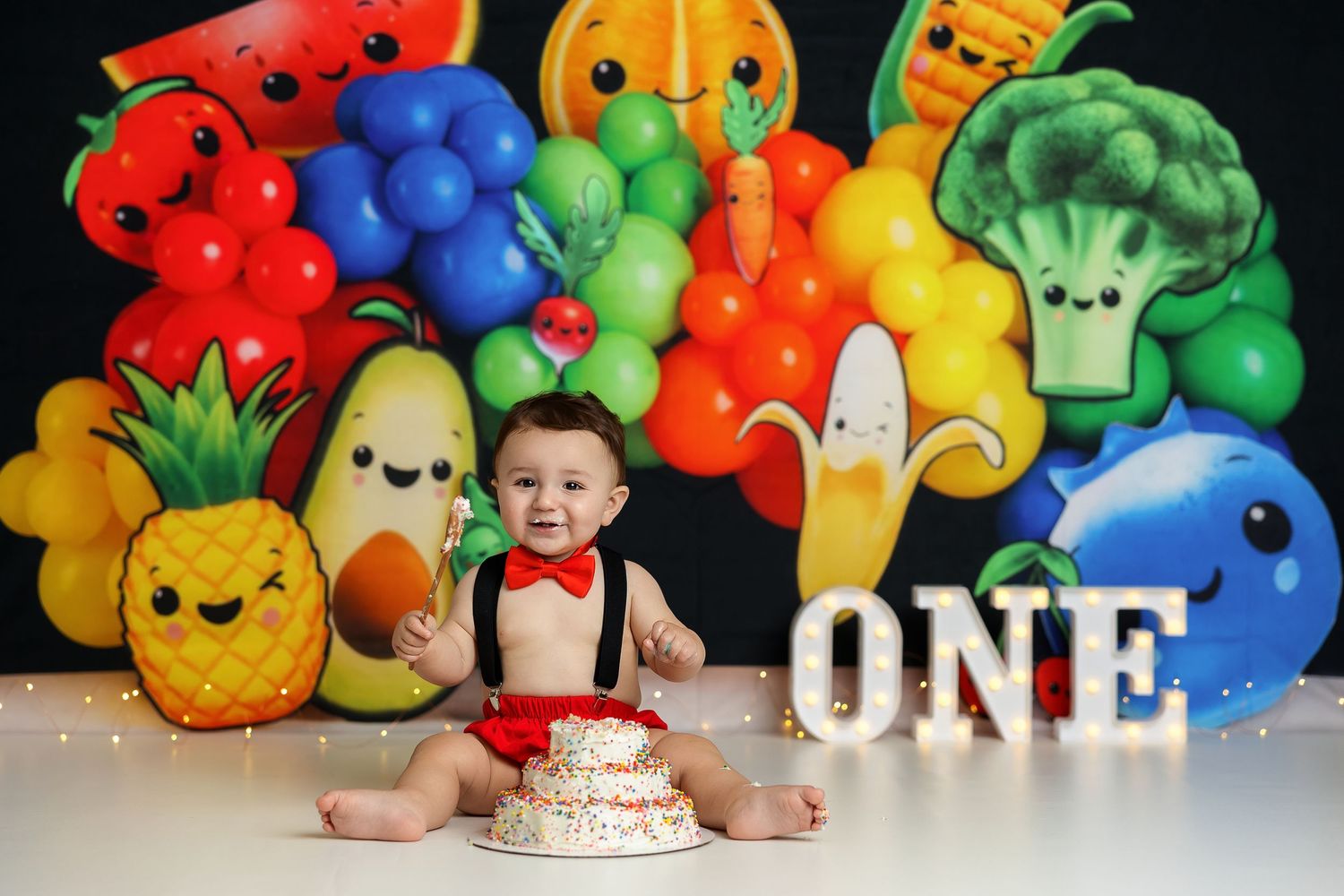 Baby's first birthday cake smash with colorful fruit and veggie balloon backdrop and ONE sign.