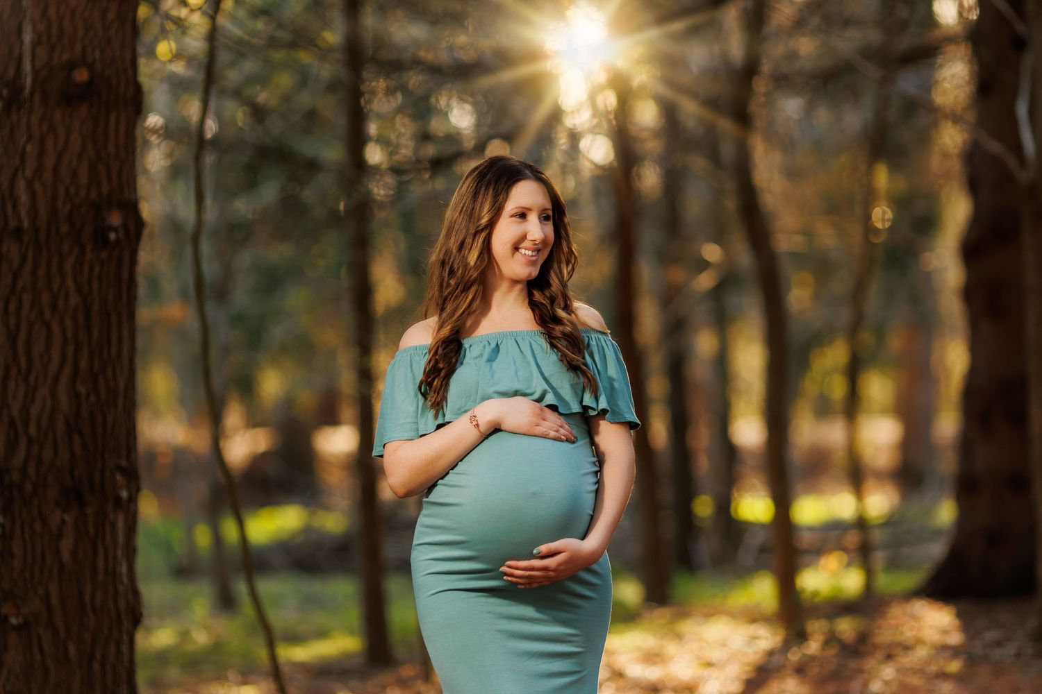 Backlit forest maternity photography session with glowing sunset through trees.