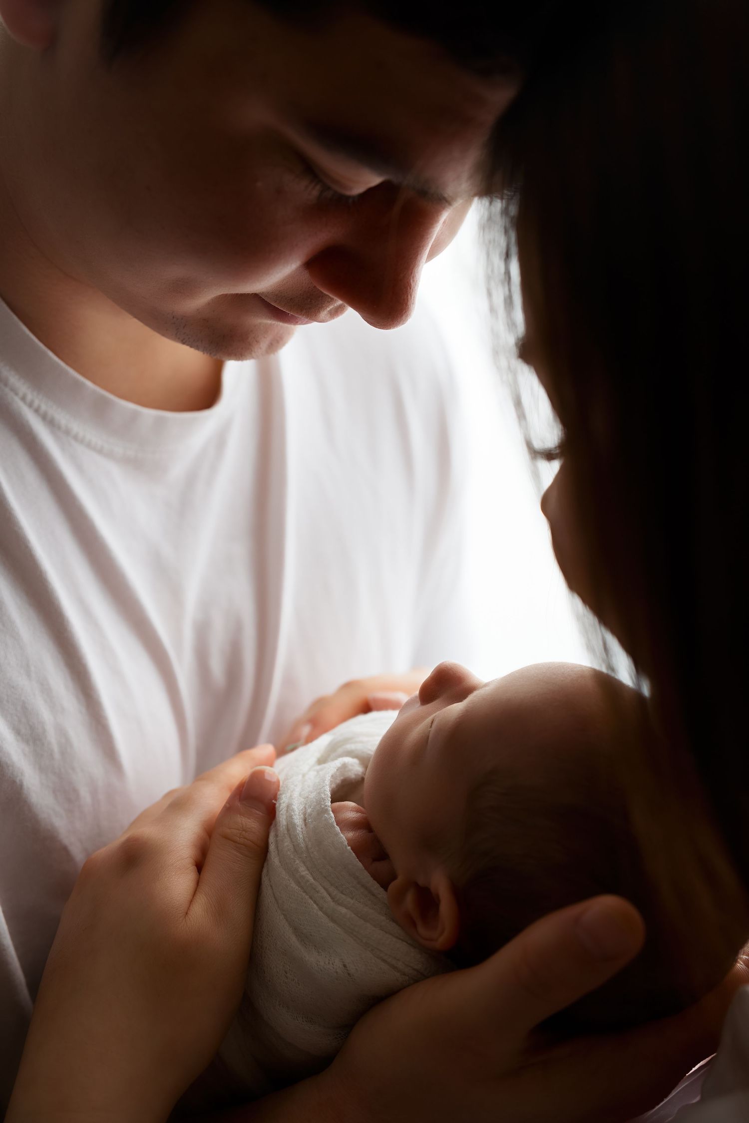 Backlit intimate portrait of parent holding sleeping newborn in gentle embrace.