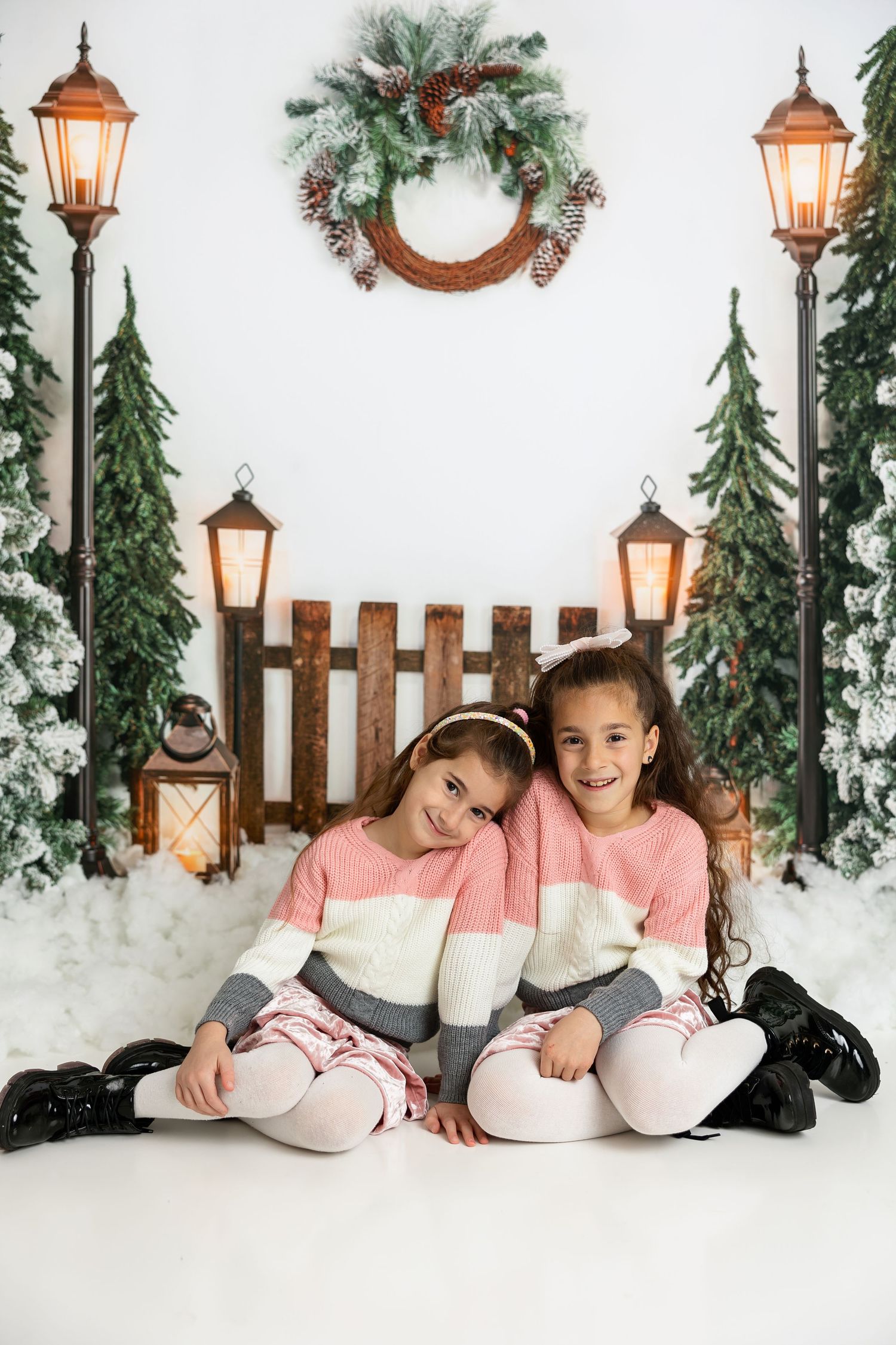 Two young children in matching pink sweaters pose in front of winter holiday scene.