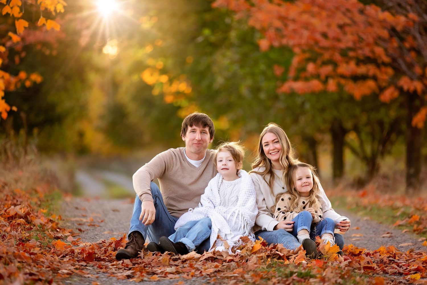 A family sits together among fallen autumn leaves during a sunset photo session.