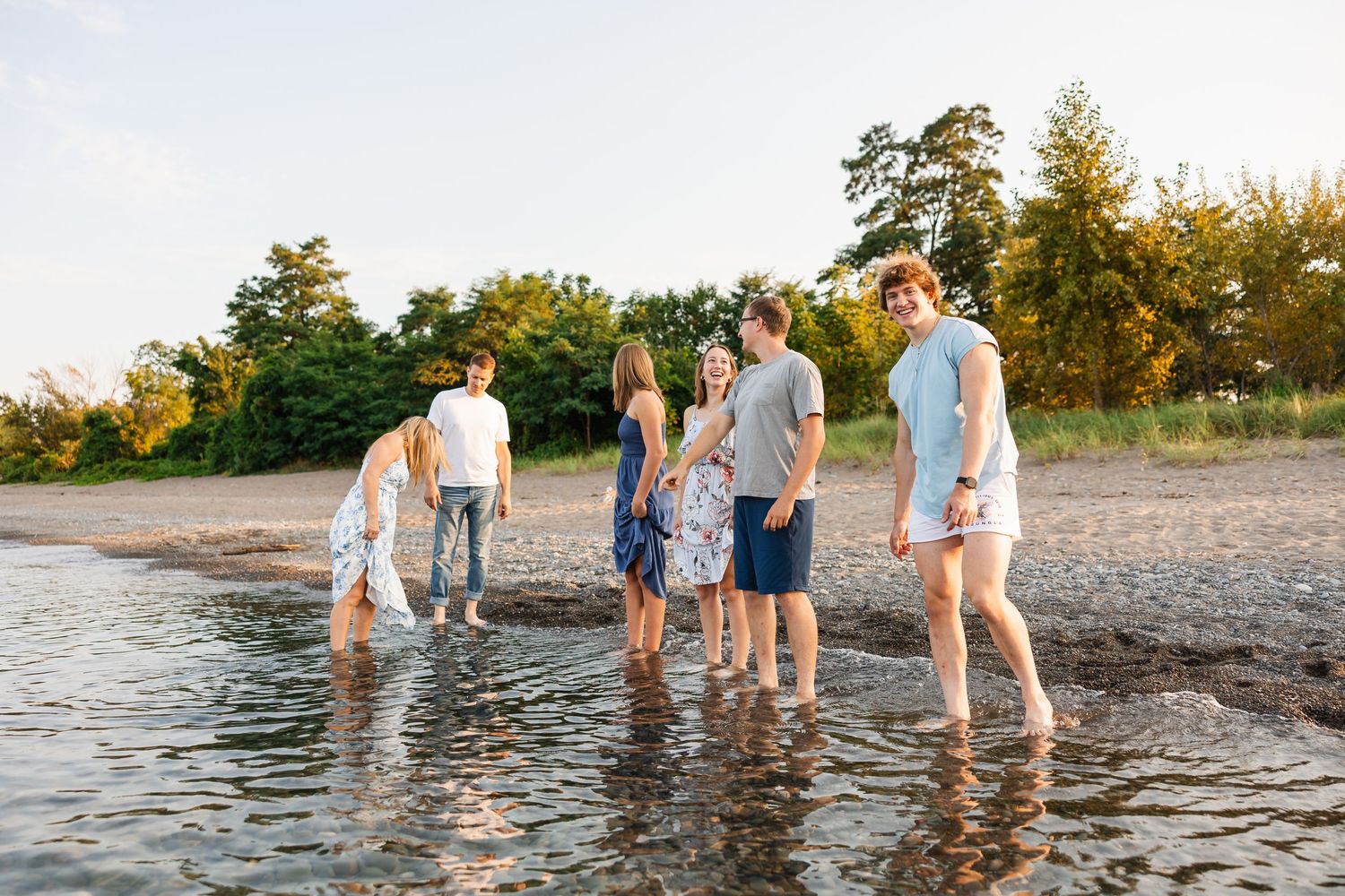 A group enjoying a summer evening at the beach as they wade together in shallow water at sunset.