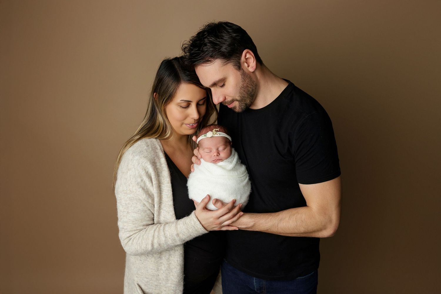 Intimate family portrait with swaddled newborn against neutral background.