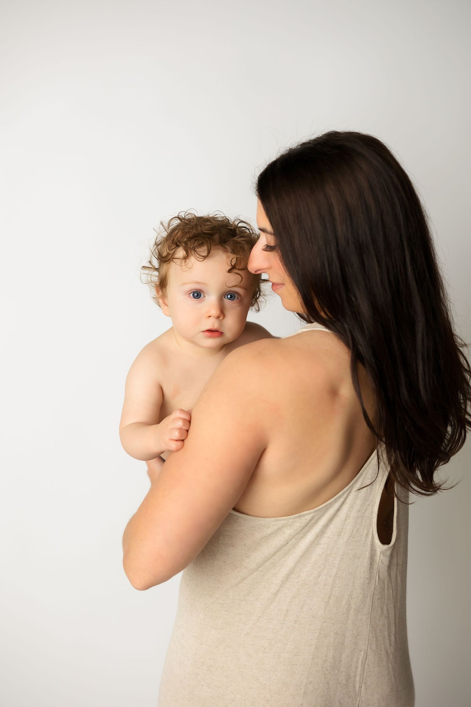 Tender moment between parent and baby against neutral background in studio portrait.
