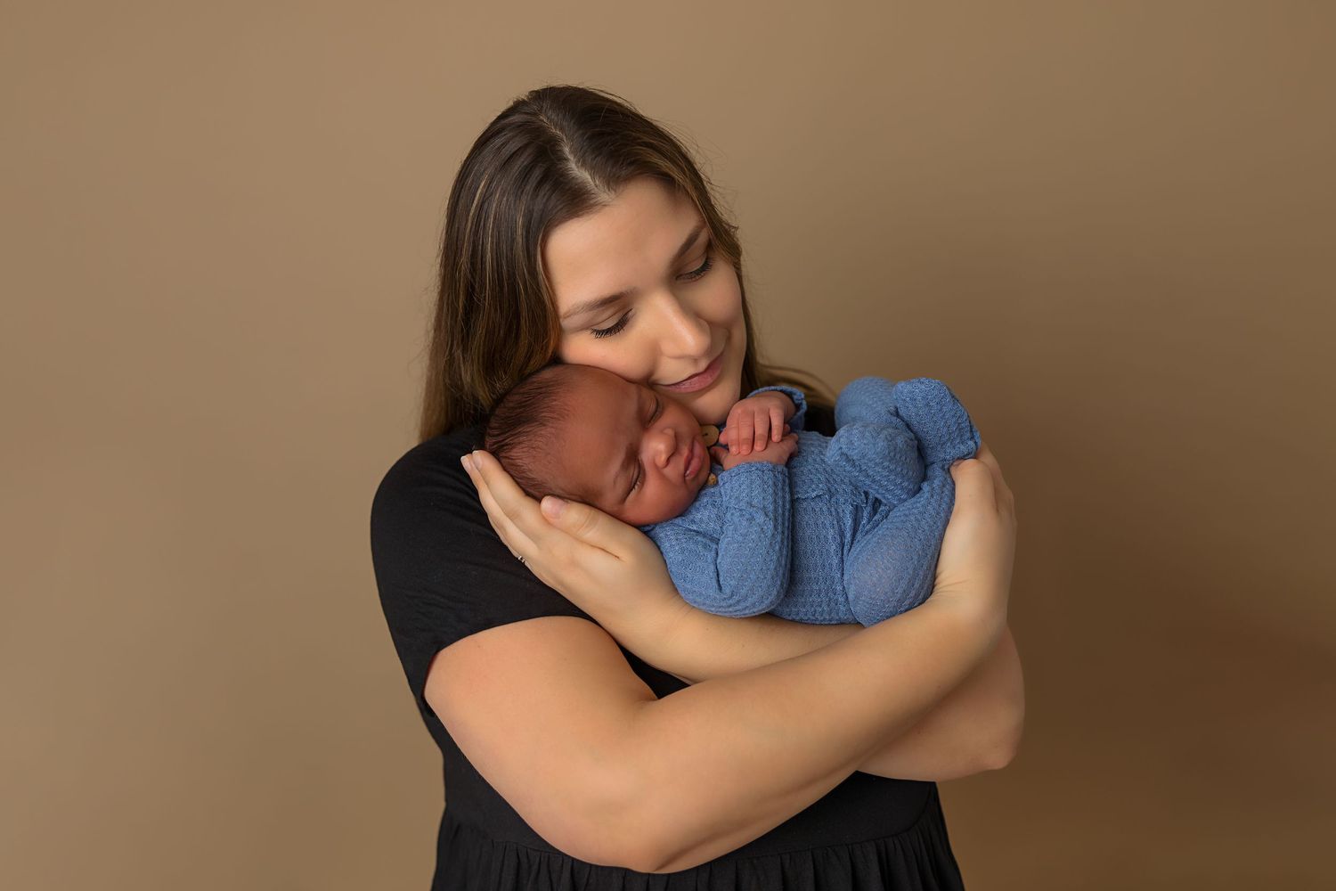 Tender moment of parent cuddling newborn dressed in blue against neutral background.