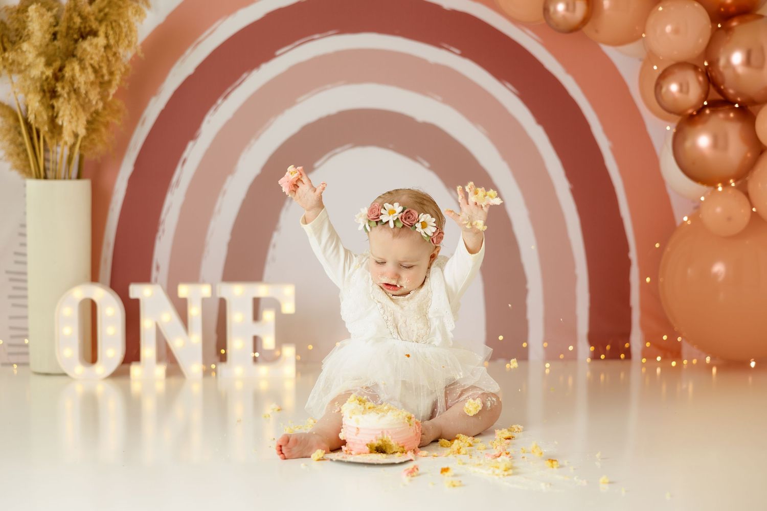 Boho-style first birthday setup with terracotta rainbow backdrop and dried pampas grass.