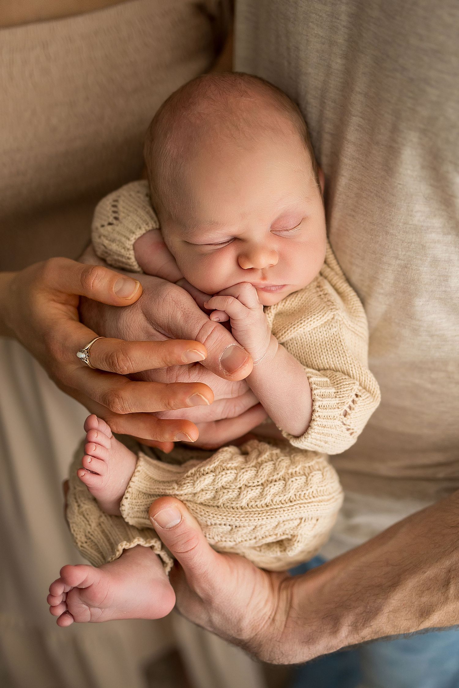 Sleeping newborn baby wrapped in cream knit blanket with tiny feet and hands visible against neutral background.
