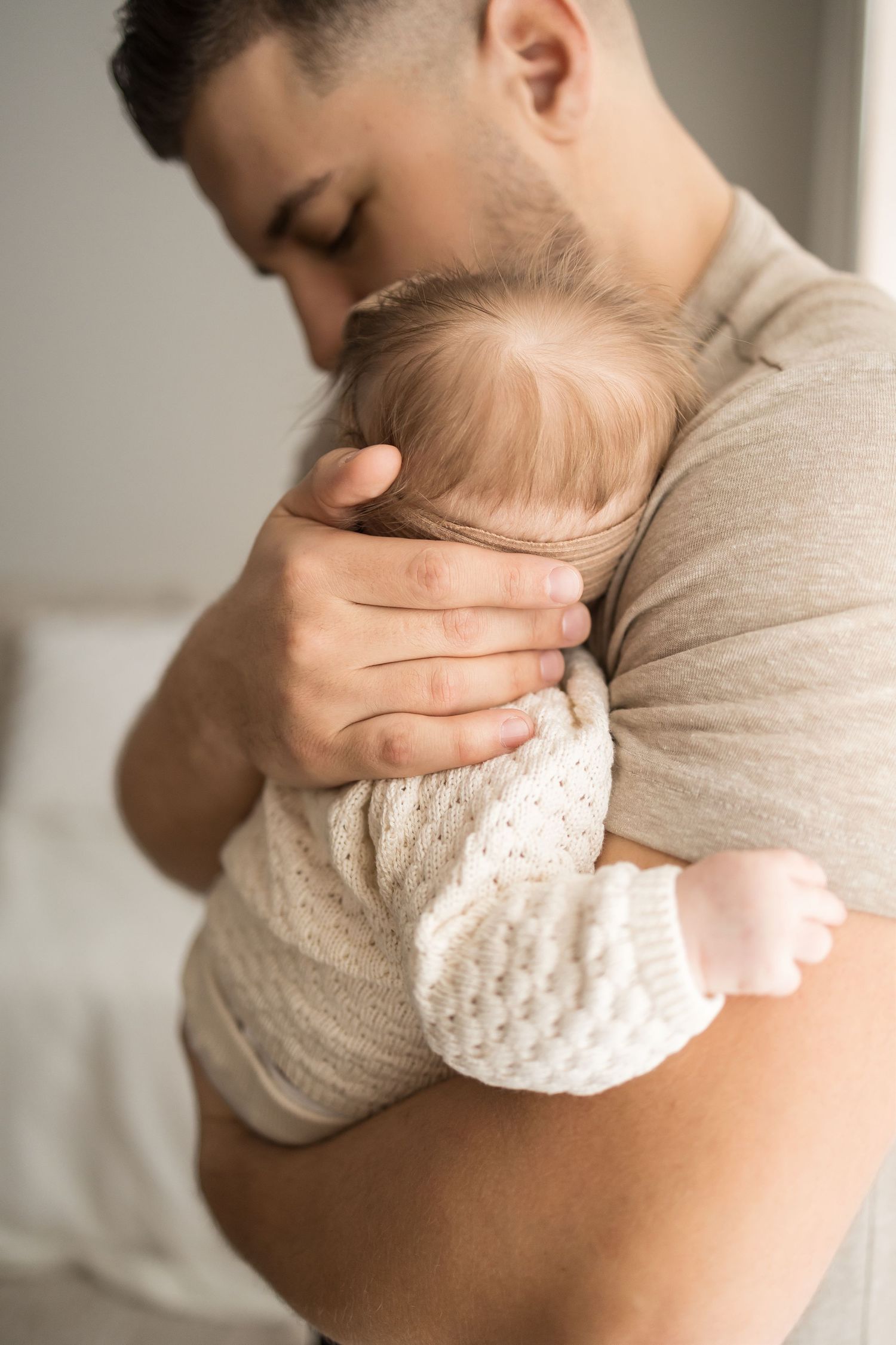 A tender moment of a father gently kissing his newborn baby dressed in a white knit outfit.