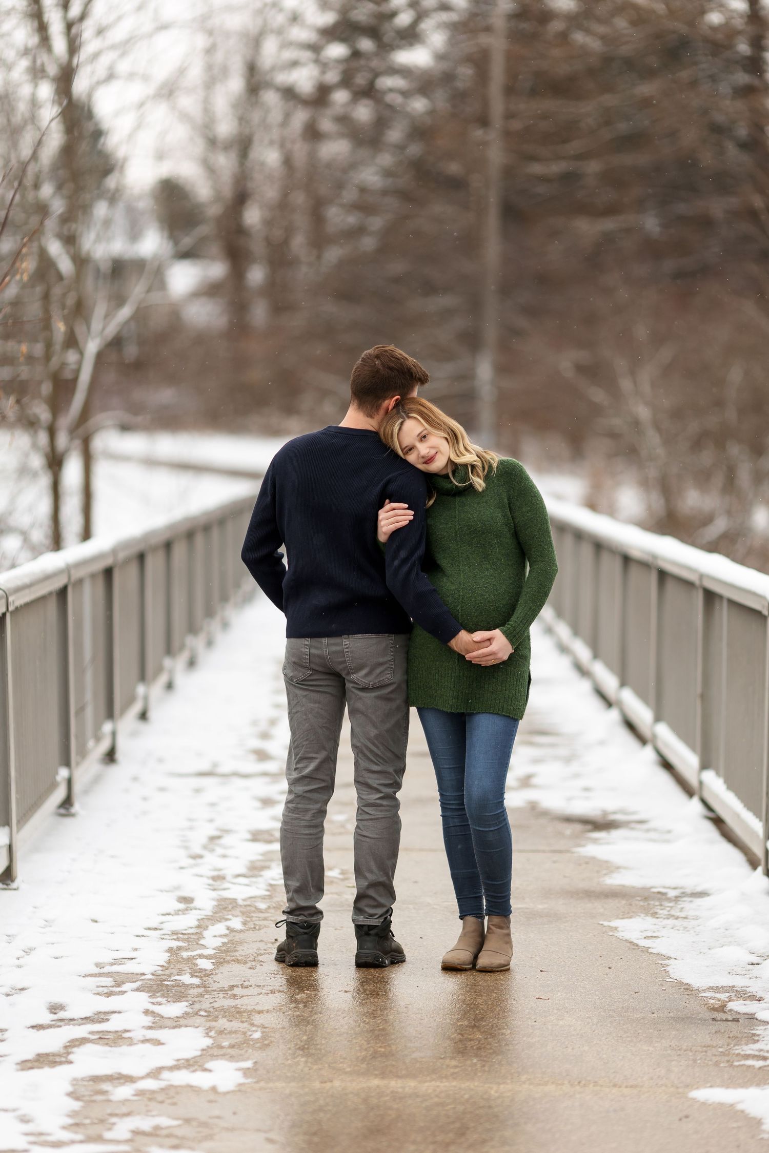 Couple sharing tender moment on snow-dusted bridge during winter photo session.