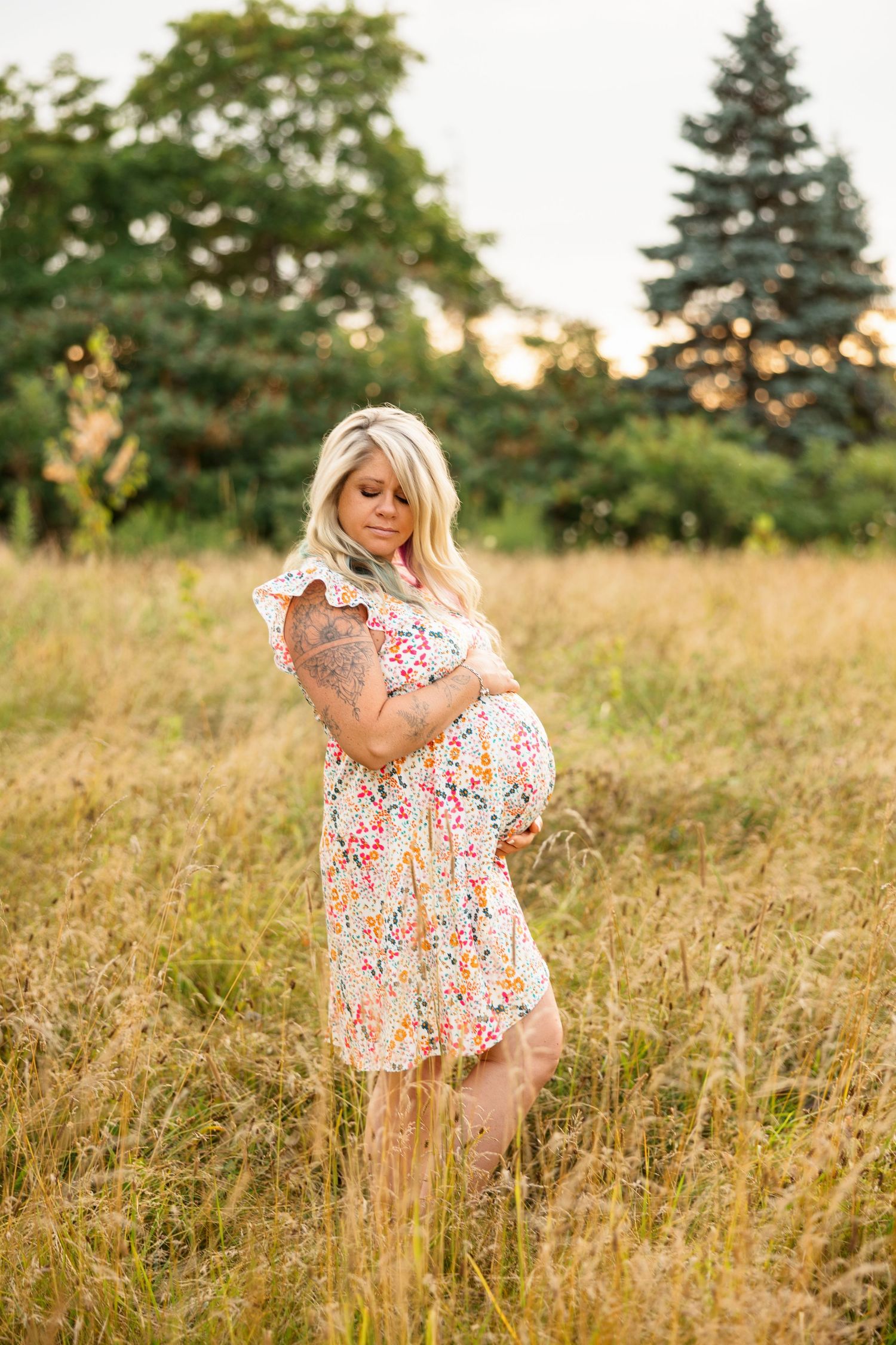 A mother and daughter in matching floral dresses stand in a sunlit field during golden hour.