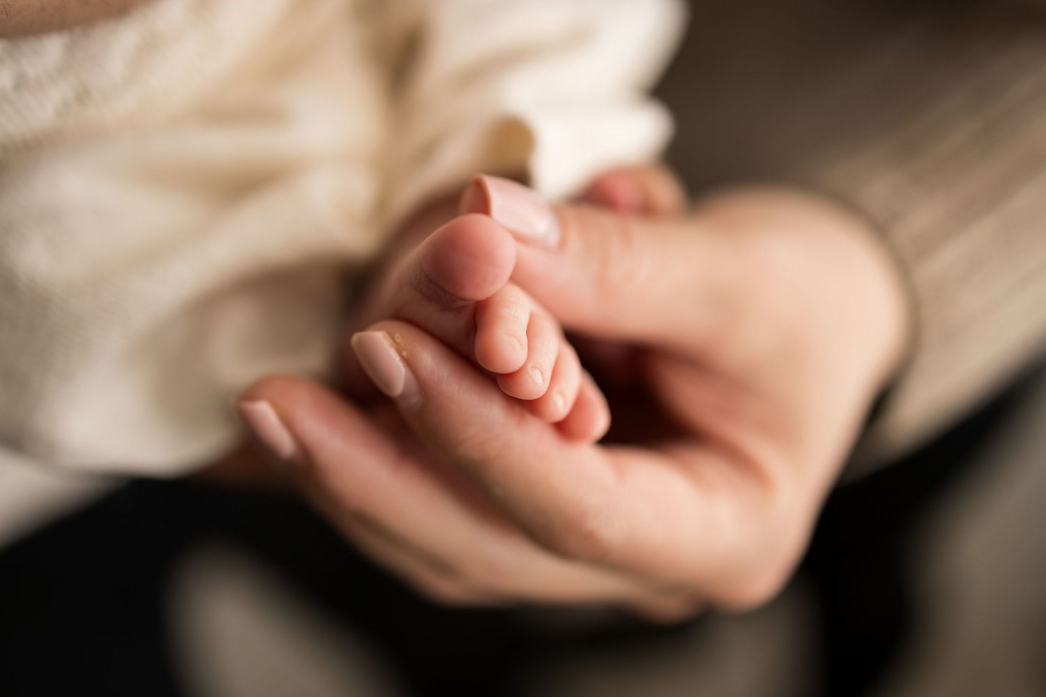 Close-up of a newborn baby's tiny hand resting gently in an adult's cupped hands.