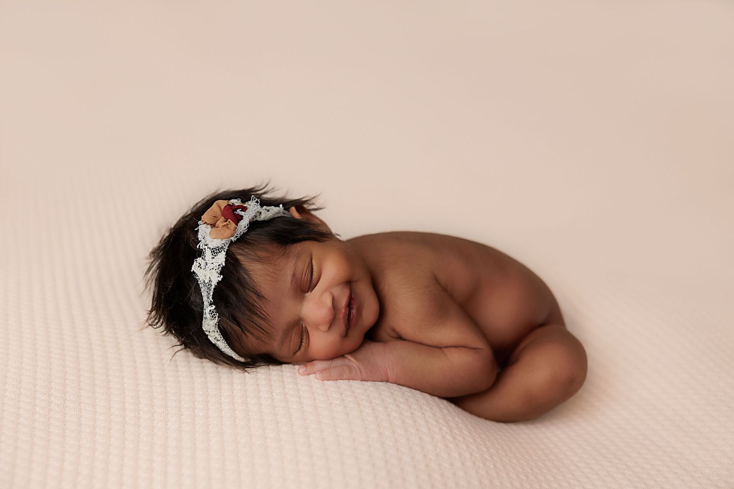 Sleeping newborn wearing delicate floral headband on cream backdrop.