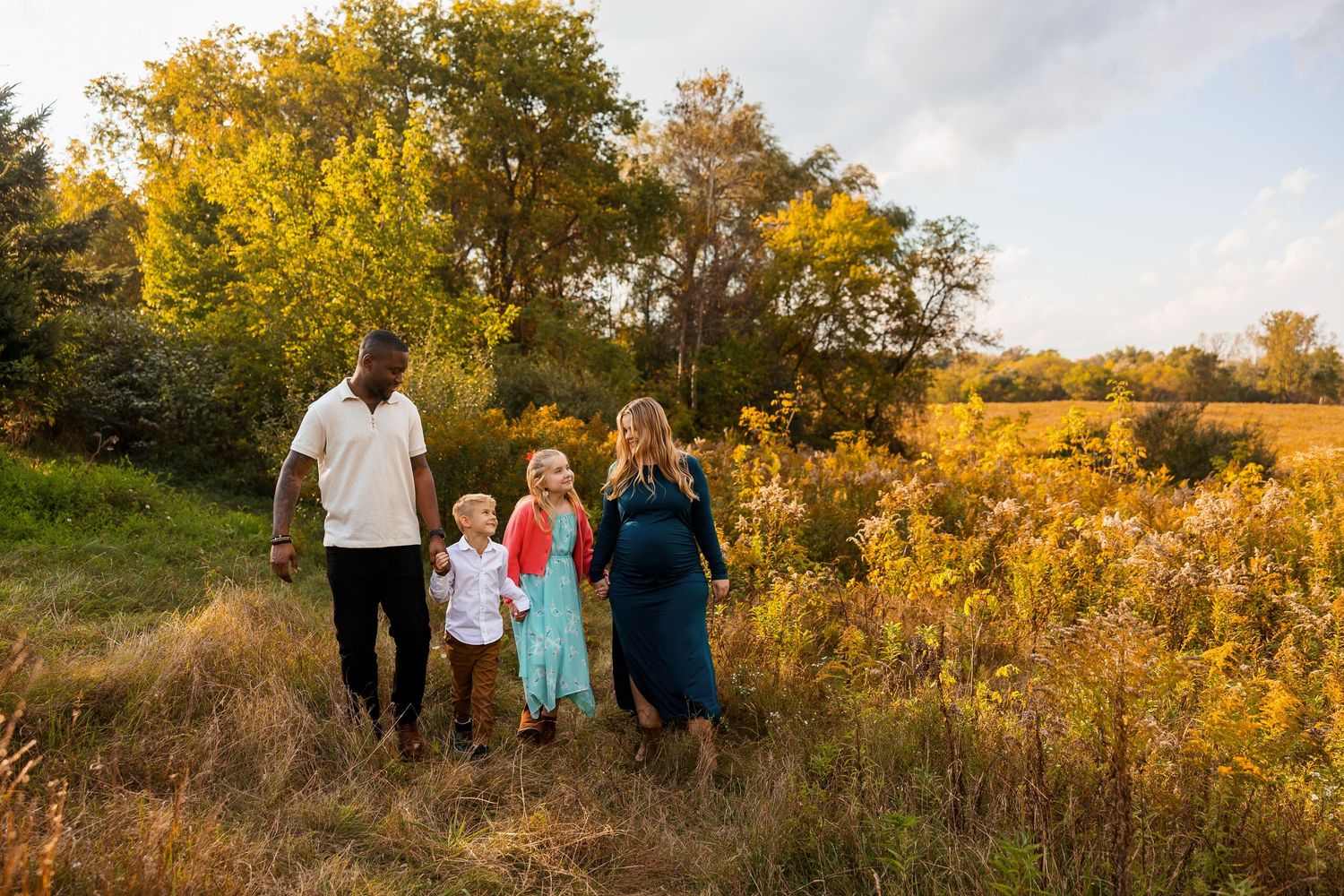 Family walks together through golden field during autumn sunset photoshoot.