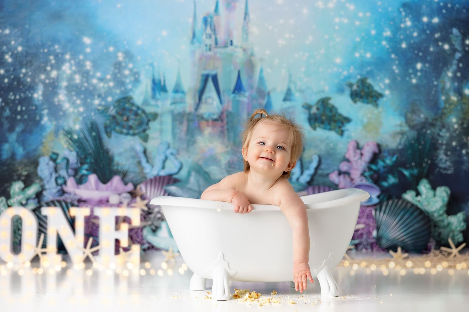 Smiling baby in white bathtub with magical castle and underwater themed backdrop.