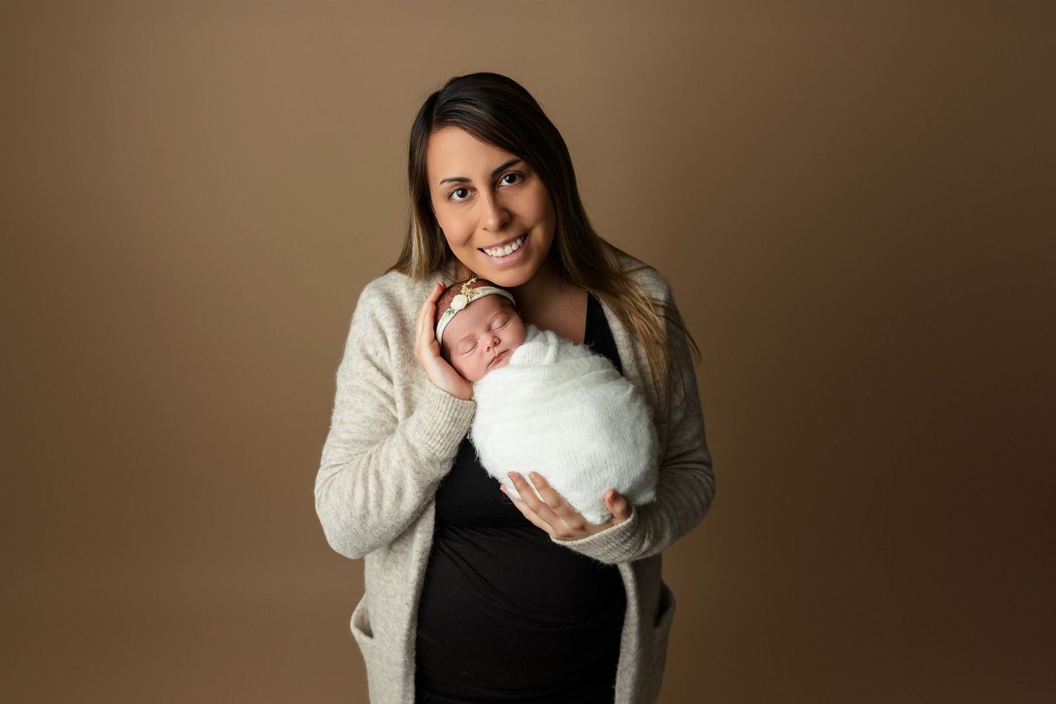 Professional studio portrait with newborn baby against warm brown background.