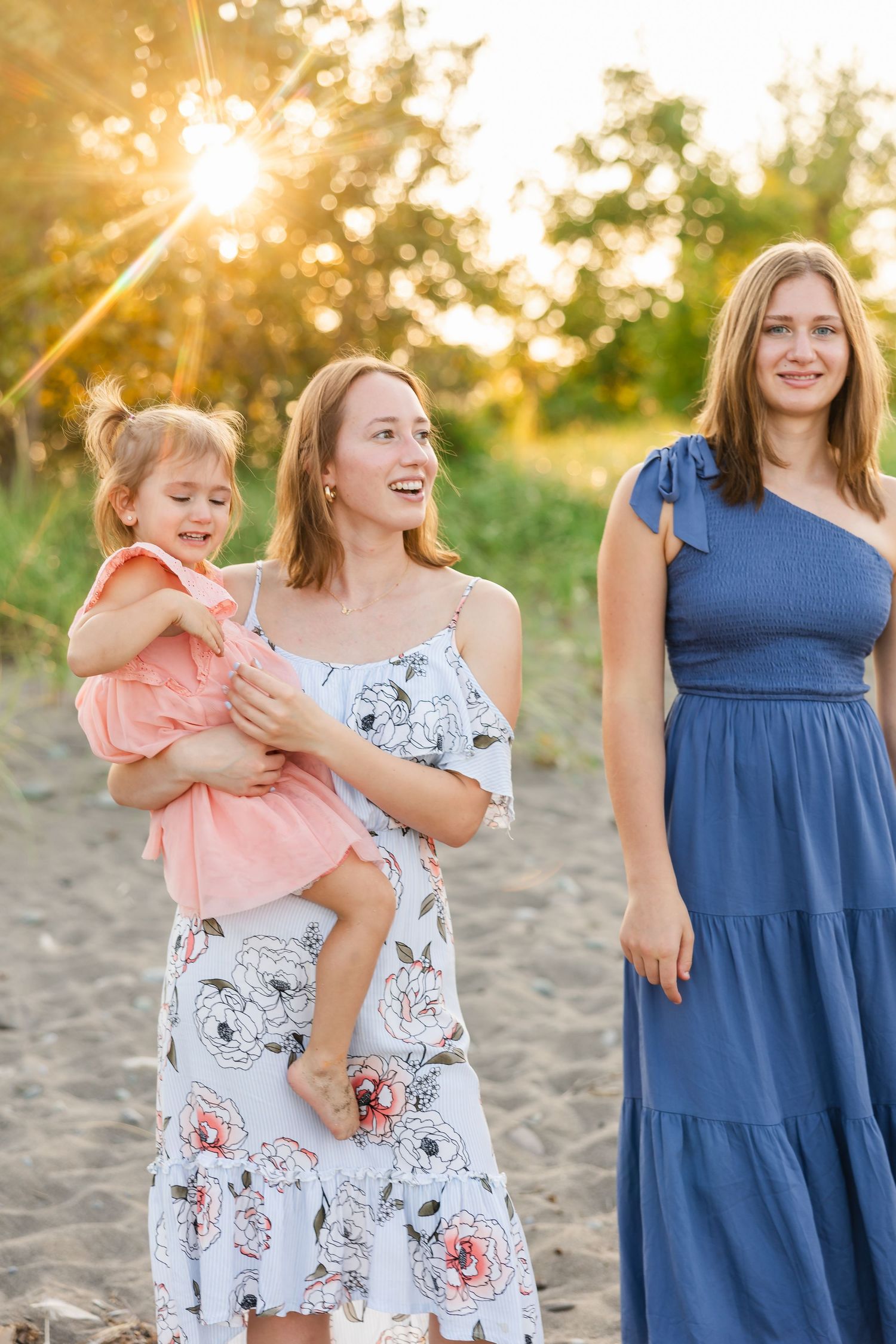 People enjoying a sunset photo session on a beach with glowing sunlight and greenery in the background.