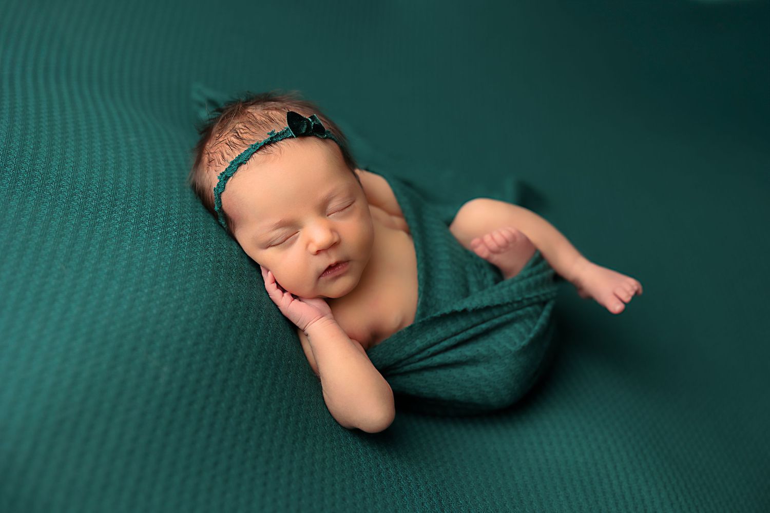 Sleeping newborn in artistic pose on teal backdrop with matching wrap.