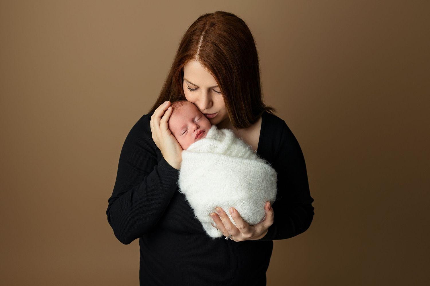 Woman in black sweater cradling swaddled newborn with tender expression.