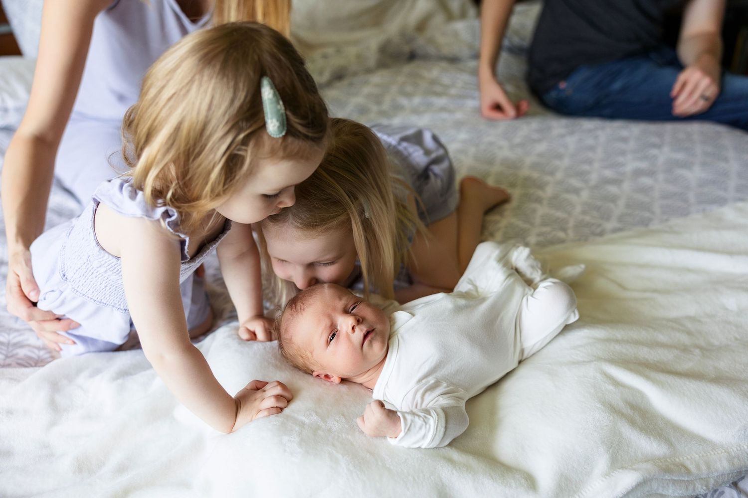 Children nestled closely together on white bedding share an intimate bonding moment.