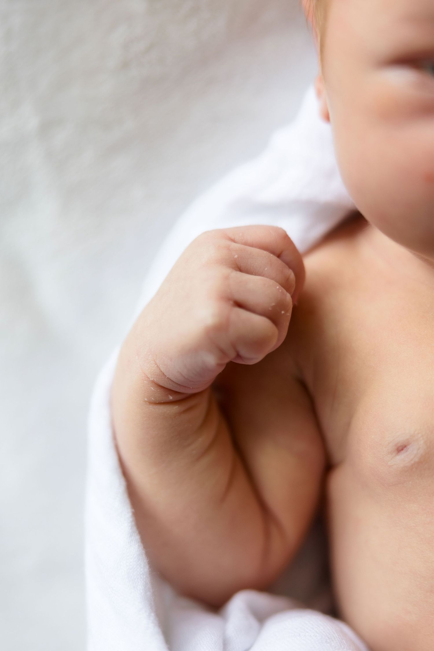 Baby's tiny hand reaching out with gentle fingers against a soft white background.