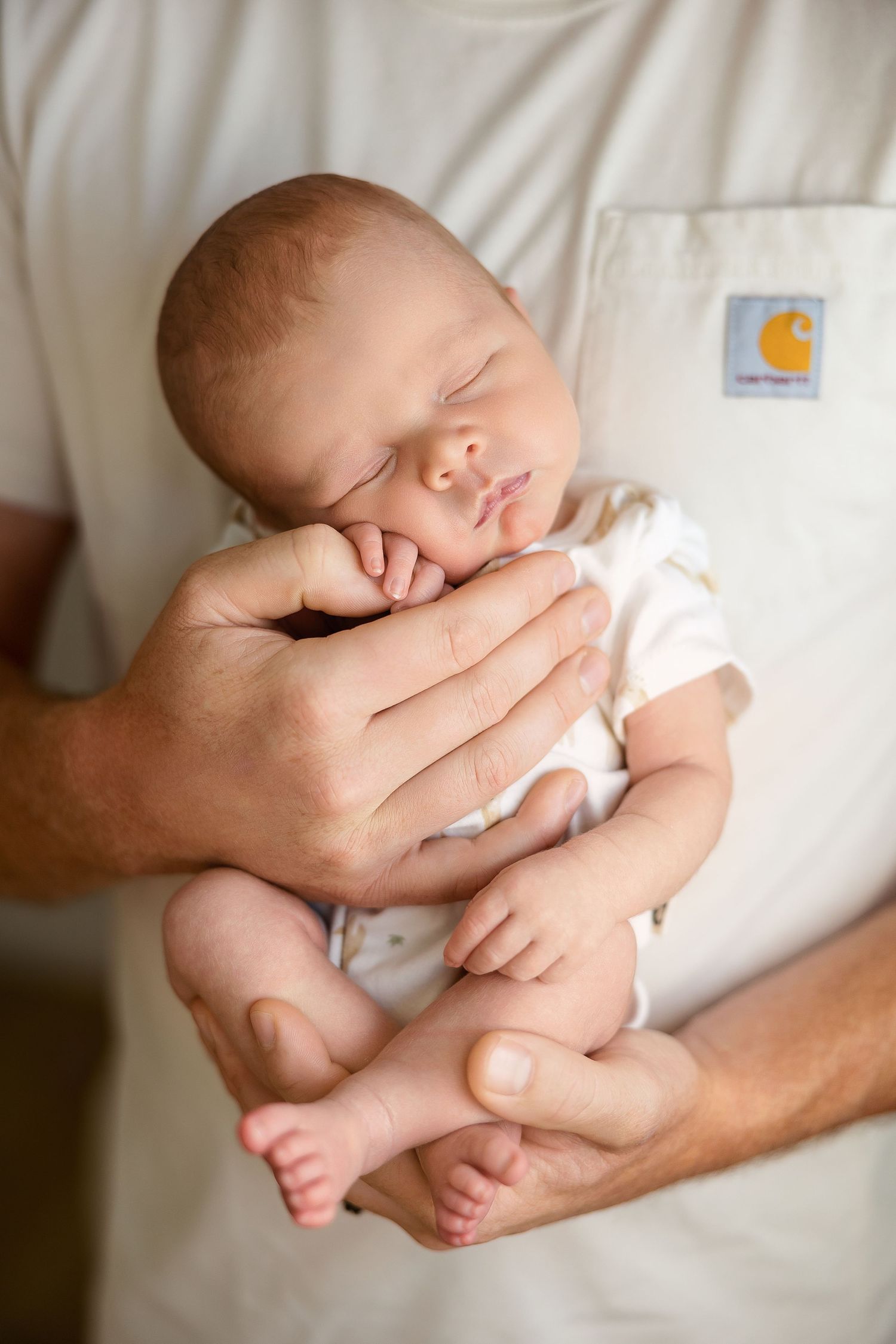 A series of gentle close-up shots showing a sleeping newborn baby cradled in caring hands against white fabric.