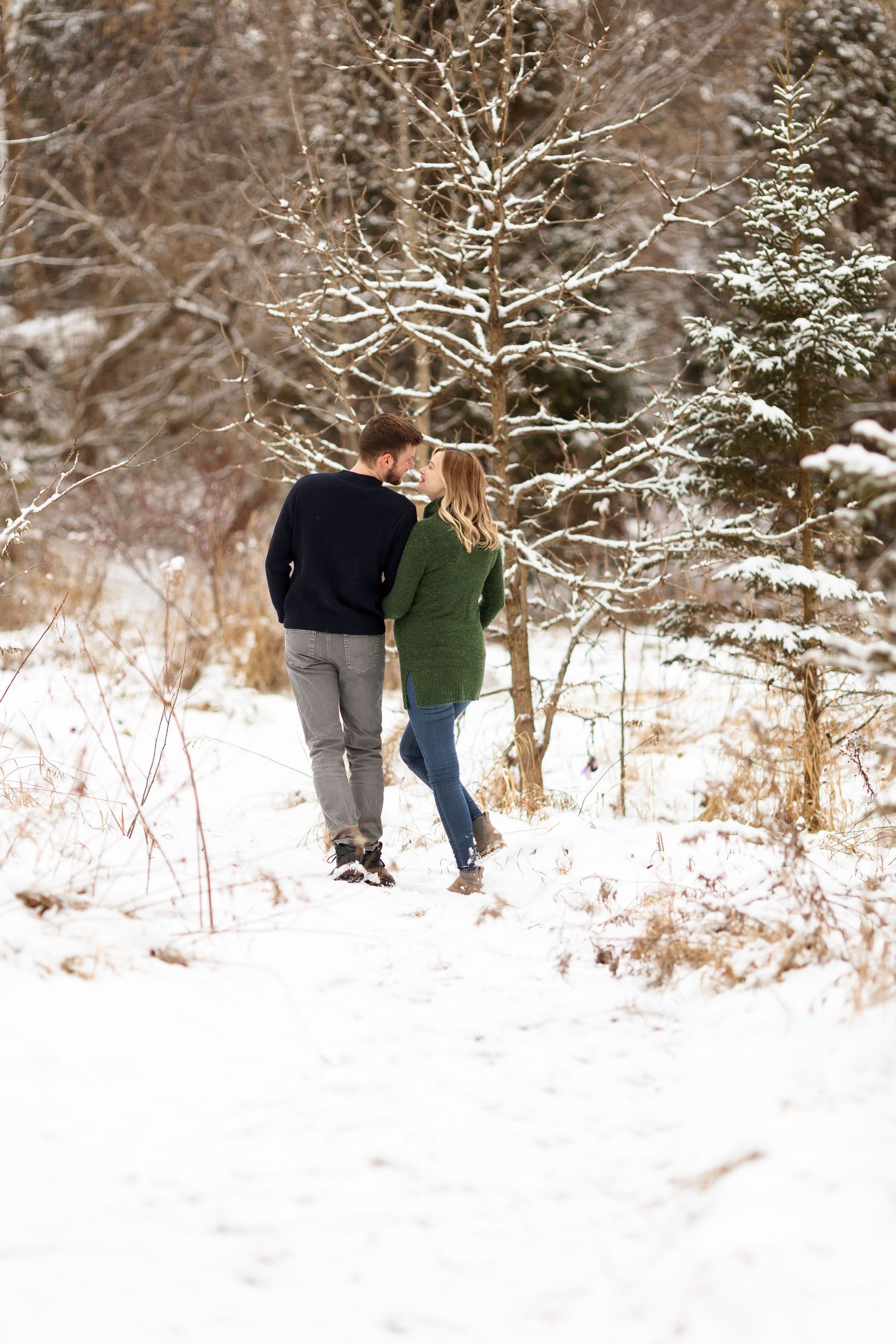 A couple strolls together on a snowy path surrounded by frost-covered trees.