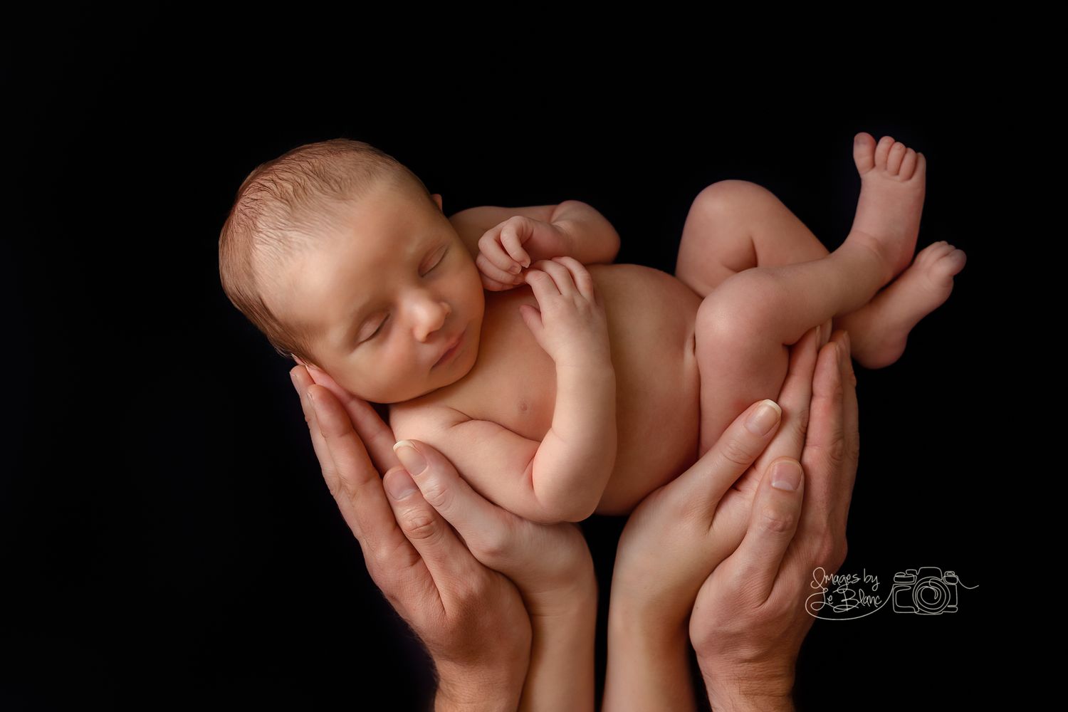 Gentle hands holding sleeping newborn baby against dark background in artistic portrait.