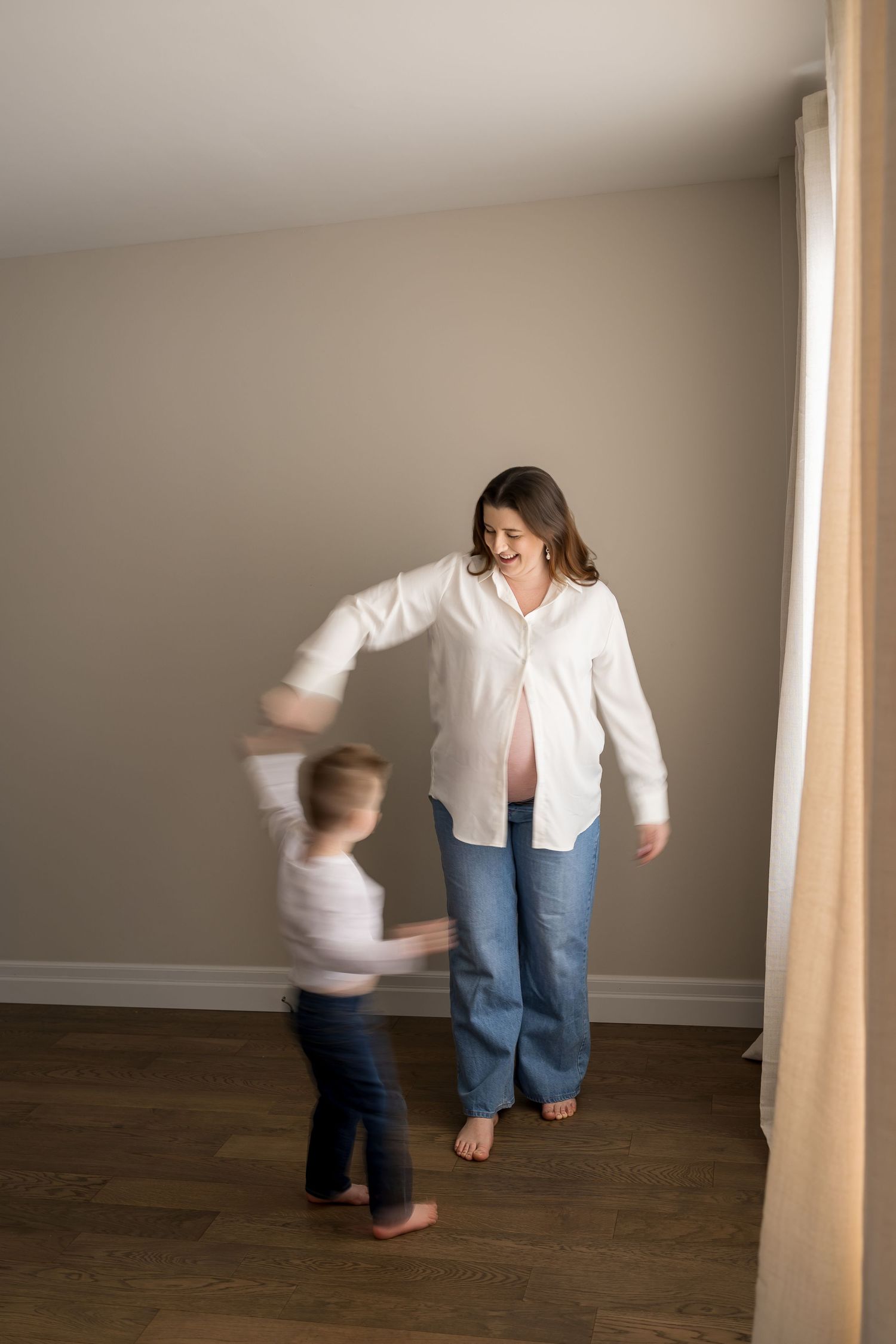 Motion blur captures playful interaction between two figures dancing on hardwood floors in a minimalist room.