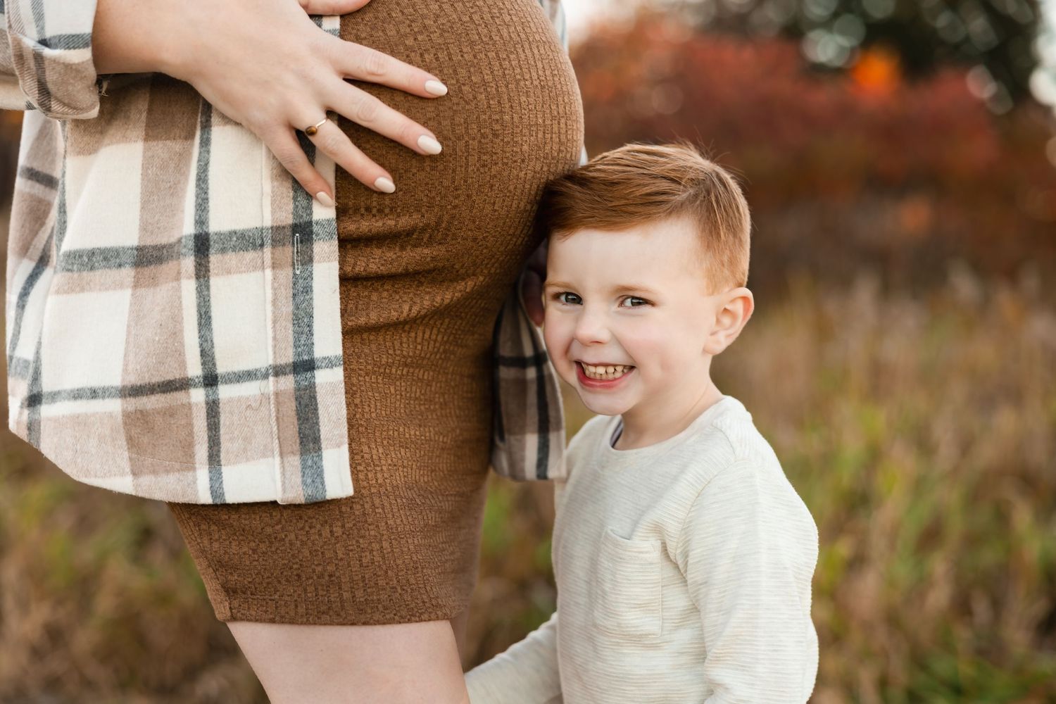 Close up of maternity moment with brown dress and plaid shirt in fall setting with child.