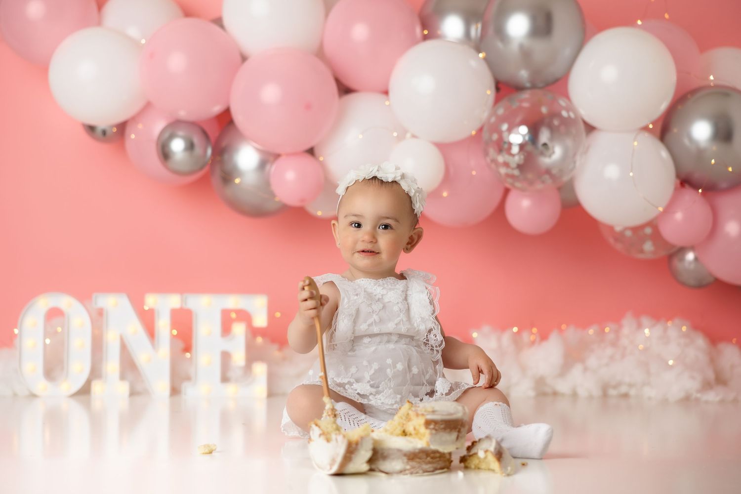 Pink and silver balloon arch with white ONE letters for first birthday celebration.