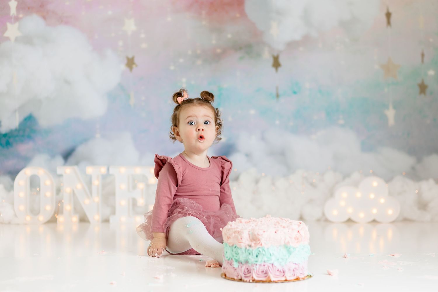 Whimsical cloud backdrop with pink and blue watercolor effect for first birthday cake smash.