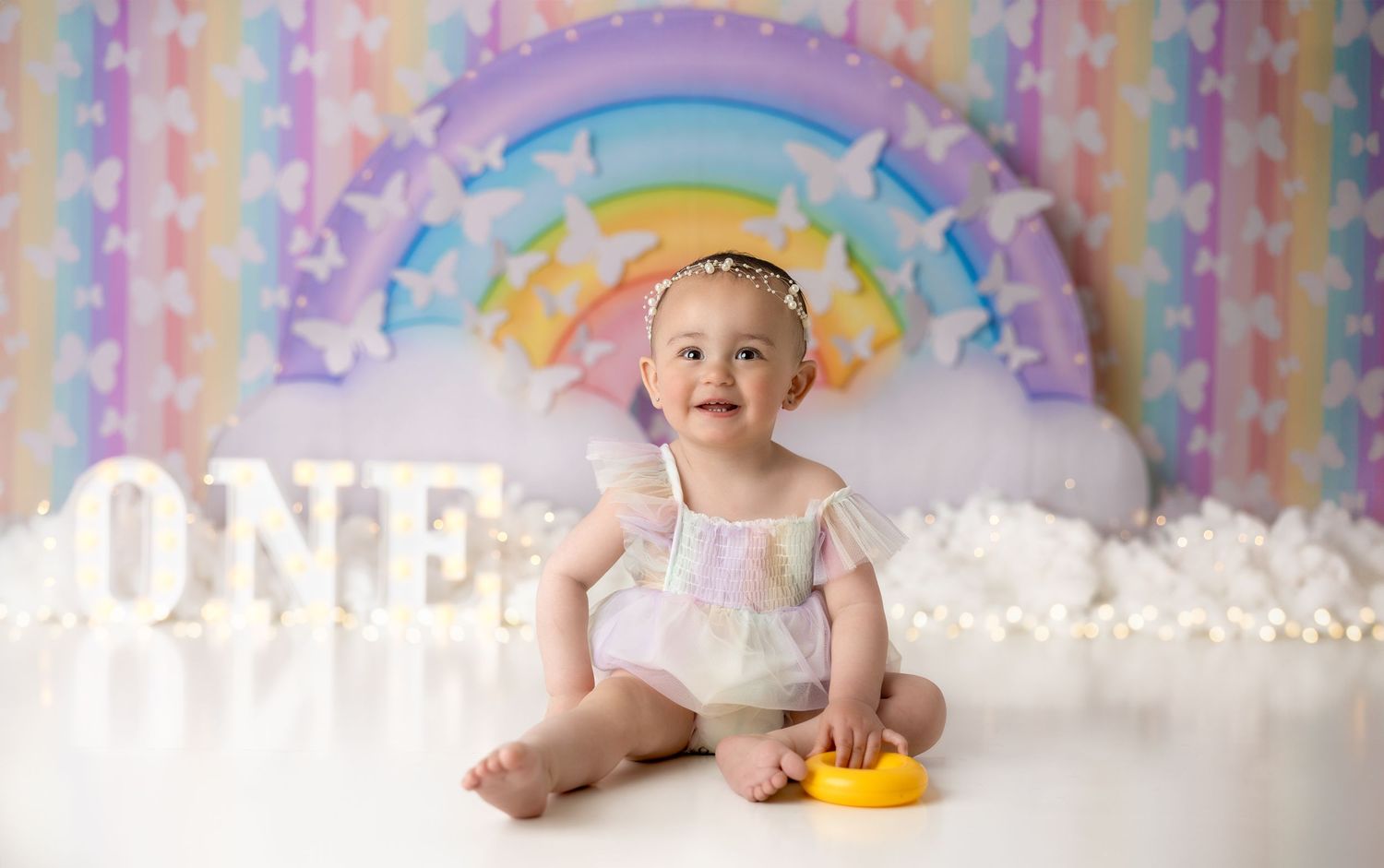 Dreamy rainbow and pastel backdrop with white fluffy decorations for first birthday photos.