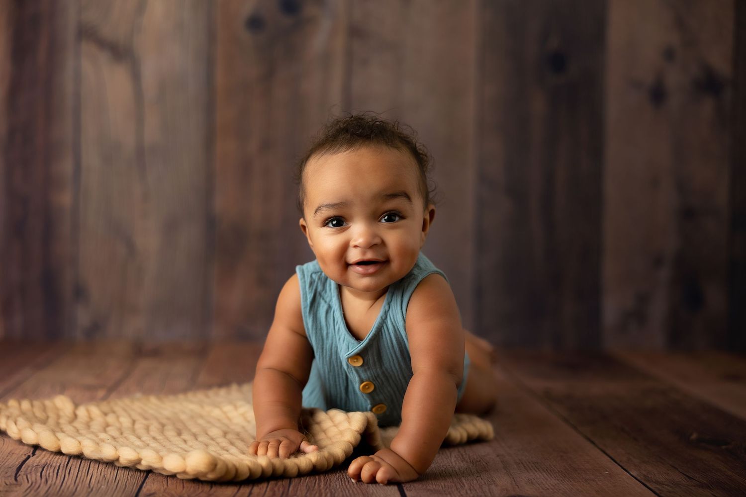 Baby wearing turquoise outfit poses against rustic wooden background.
