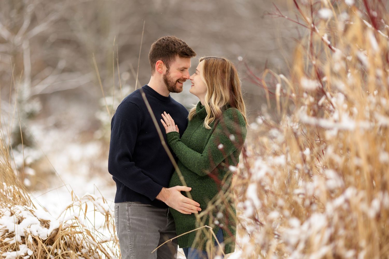 A romantic winter maternity photoshoot among dried tall grasses and snow.