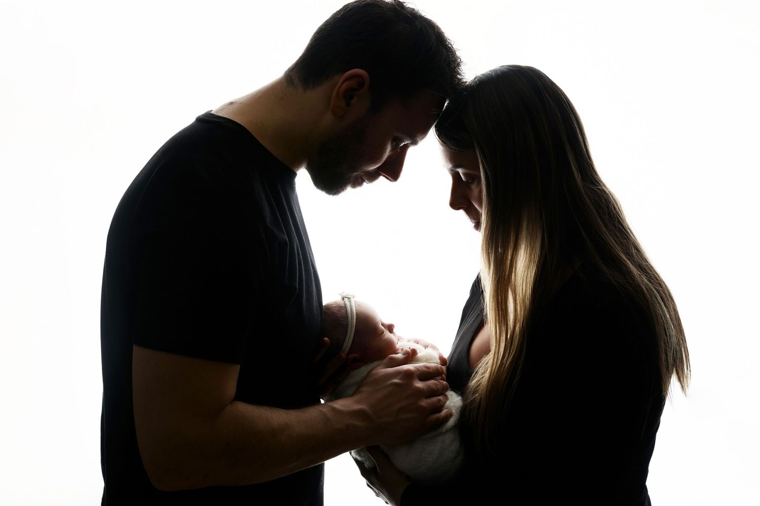 Silhouetted family portrait with newborn in dramatic lighting.