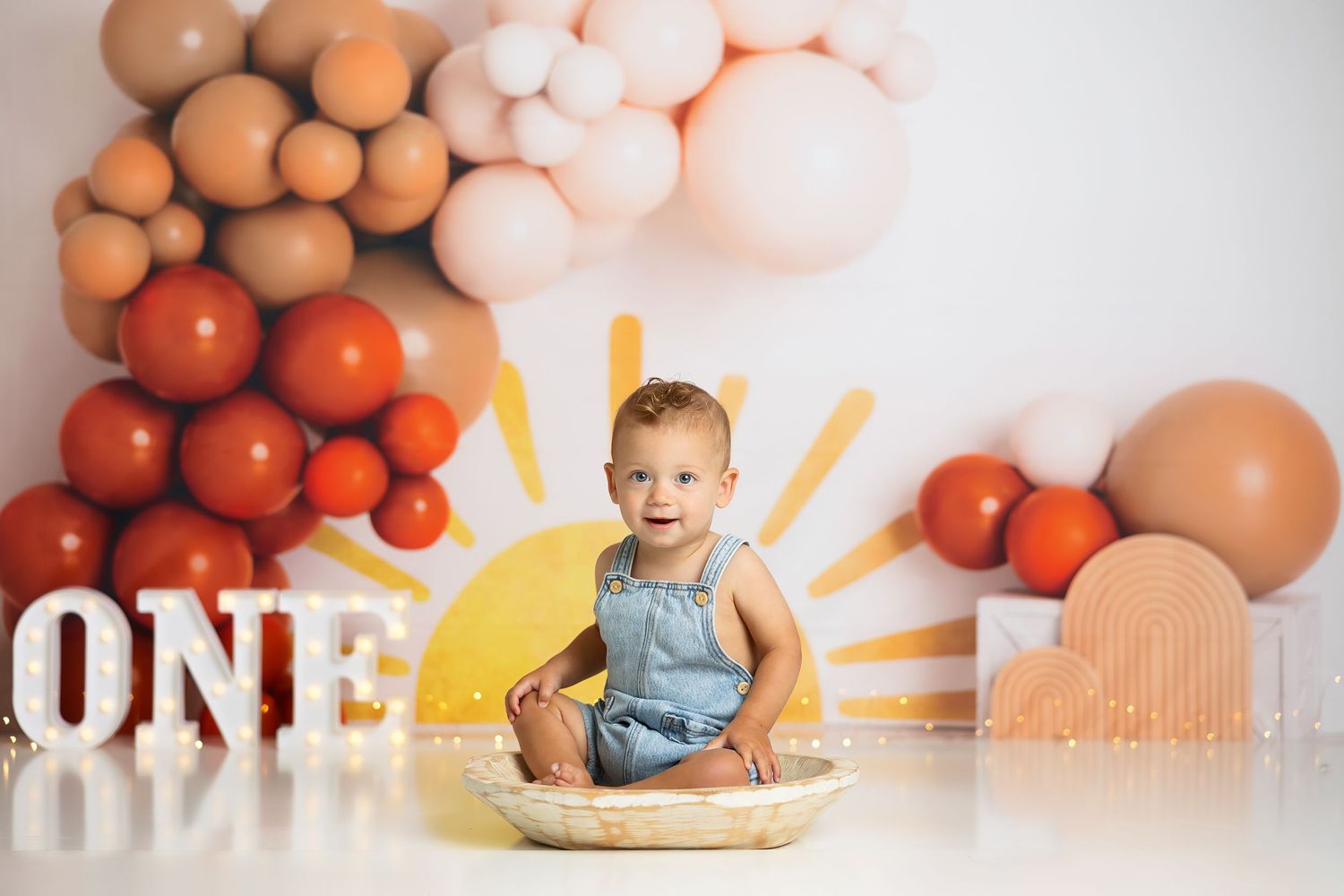 First birthday photo with white letter decorations and colorful balloon arrangements.