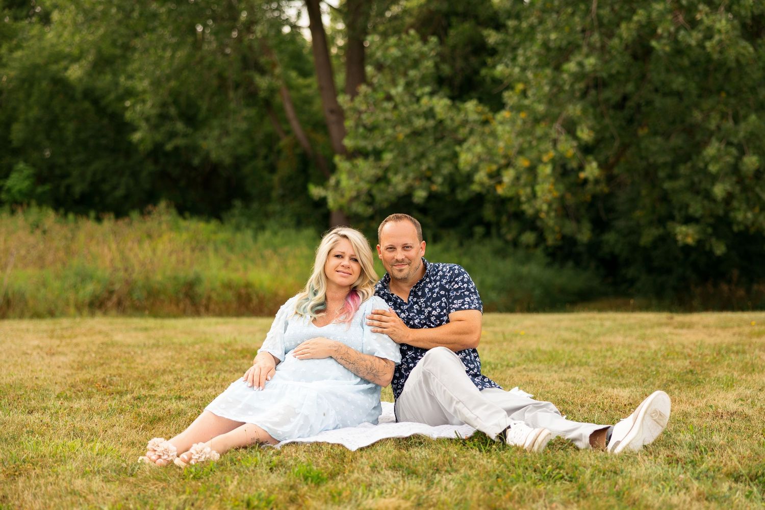 Couple relaxing together on grass during sunny outdoor photoshoot in park setting.