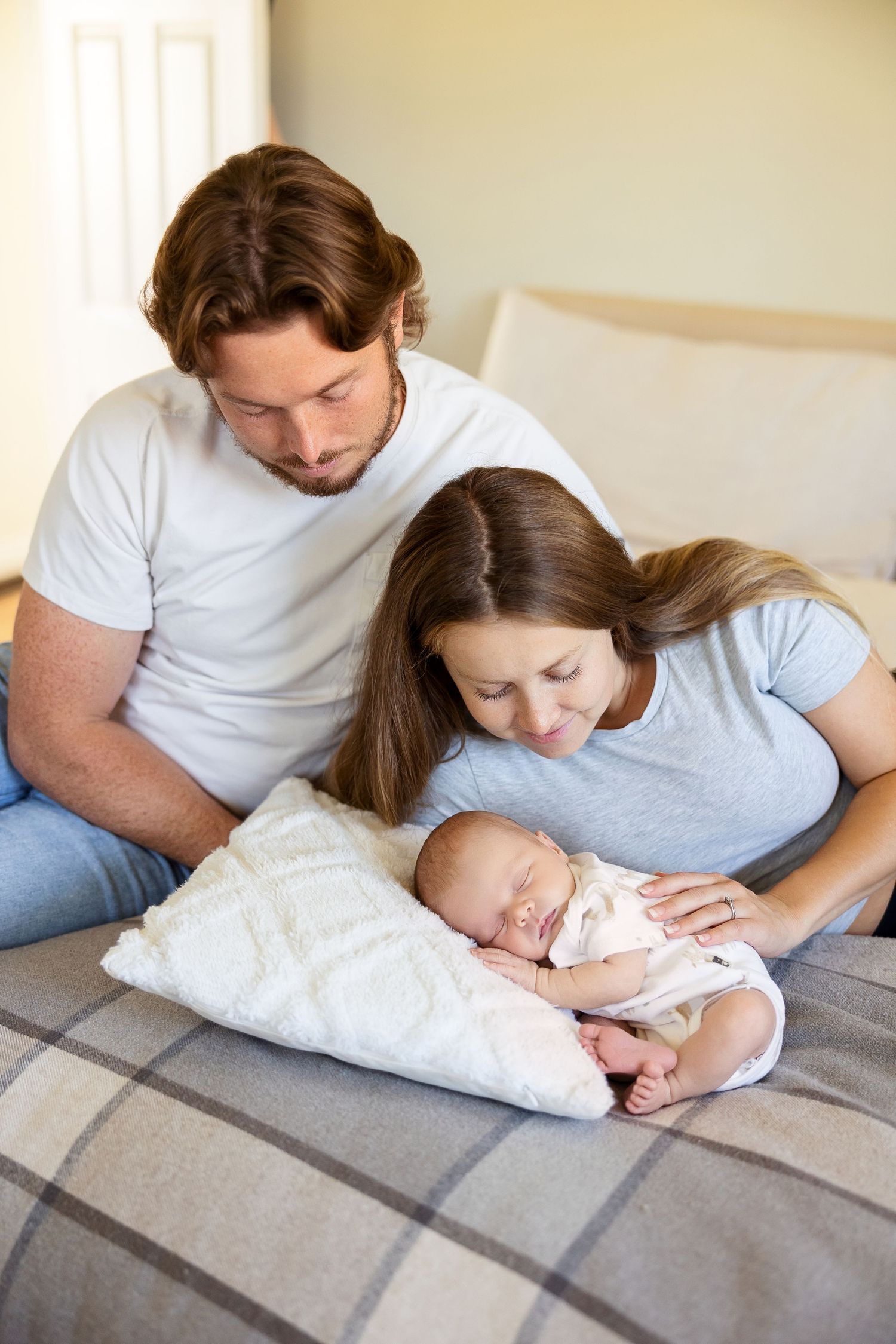 A series of intimate family moments on a gray blanket showing parents bonding with their sleeping newborn.