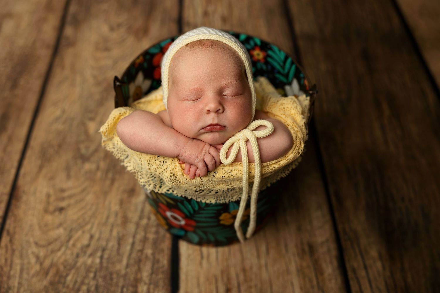 Sleeping newborn in floral patterned bowl with cream colored padding.