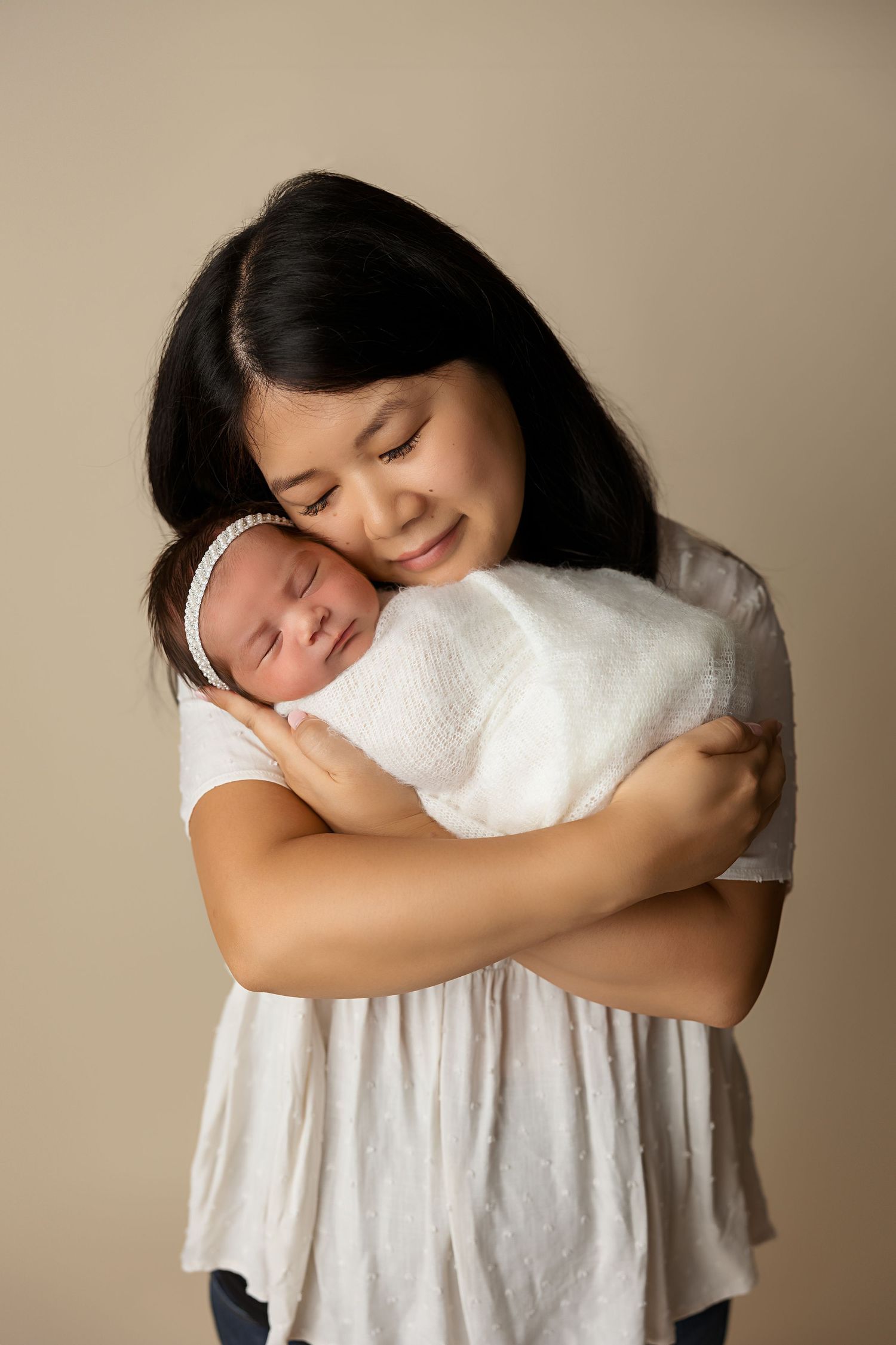 An intimate newborn photography moment against a simple beige background.