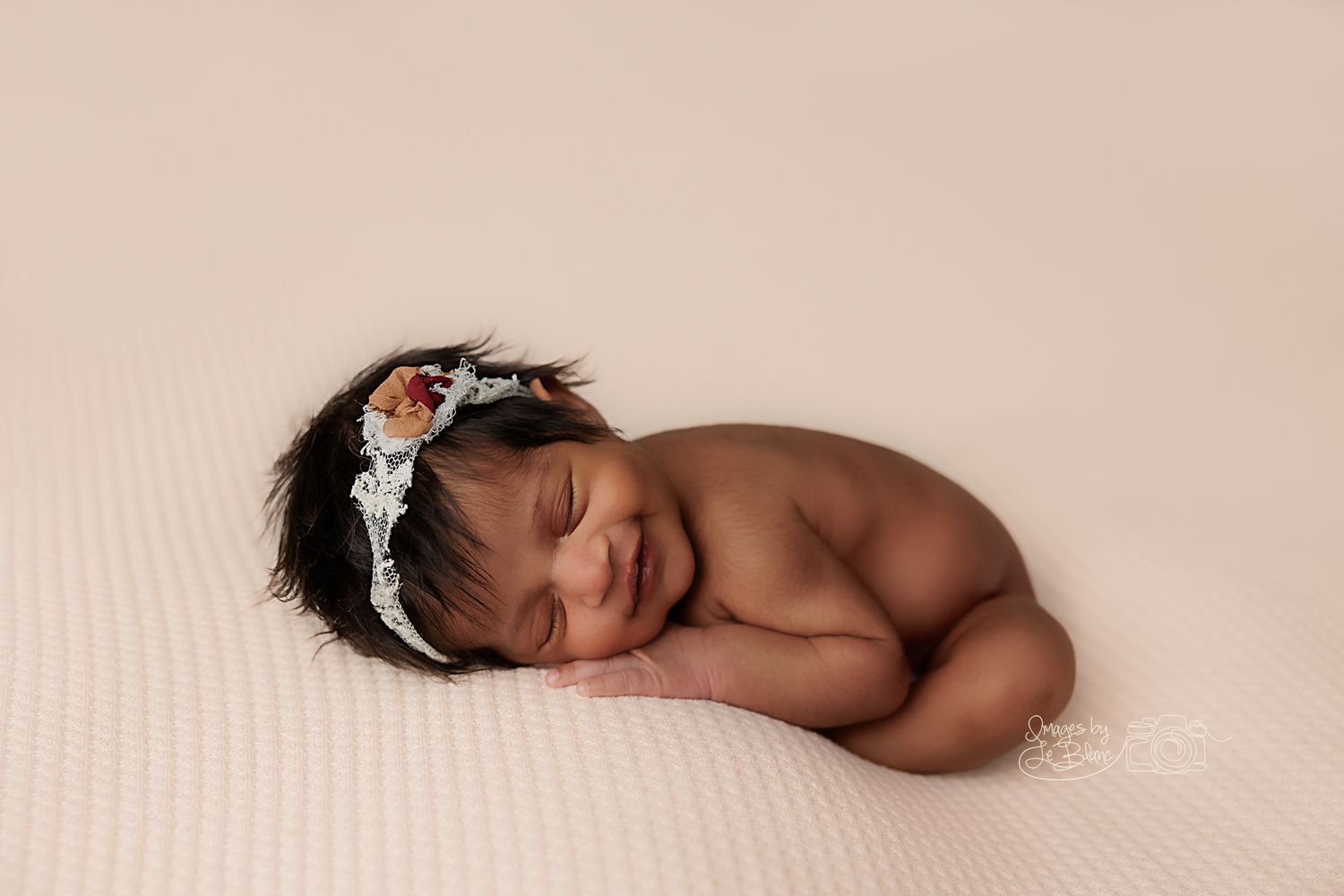 Peaceful sleeping newborn wearing delicate silver headband on beige backdrop.
