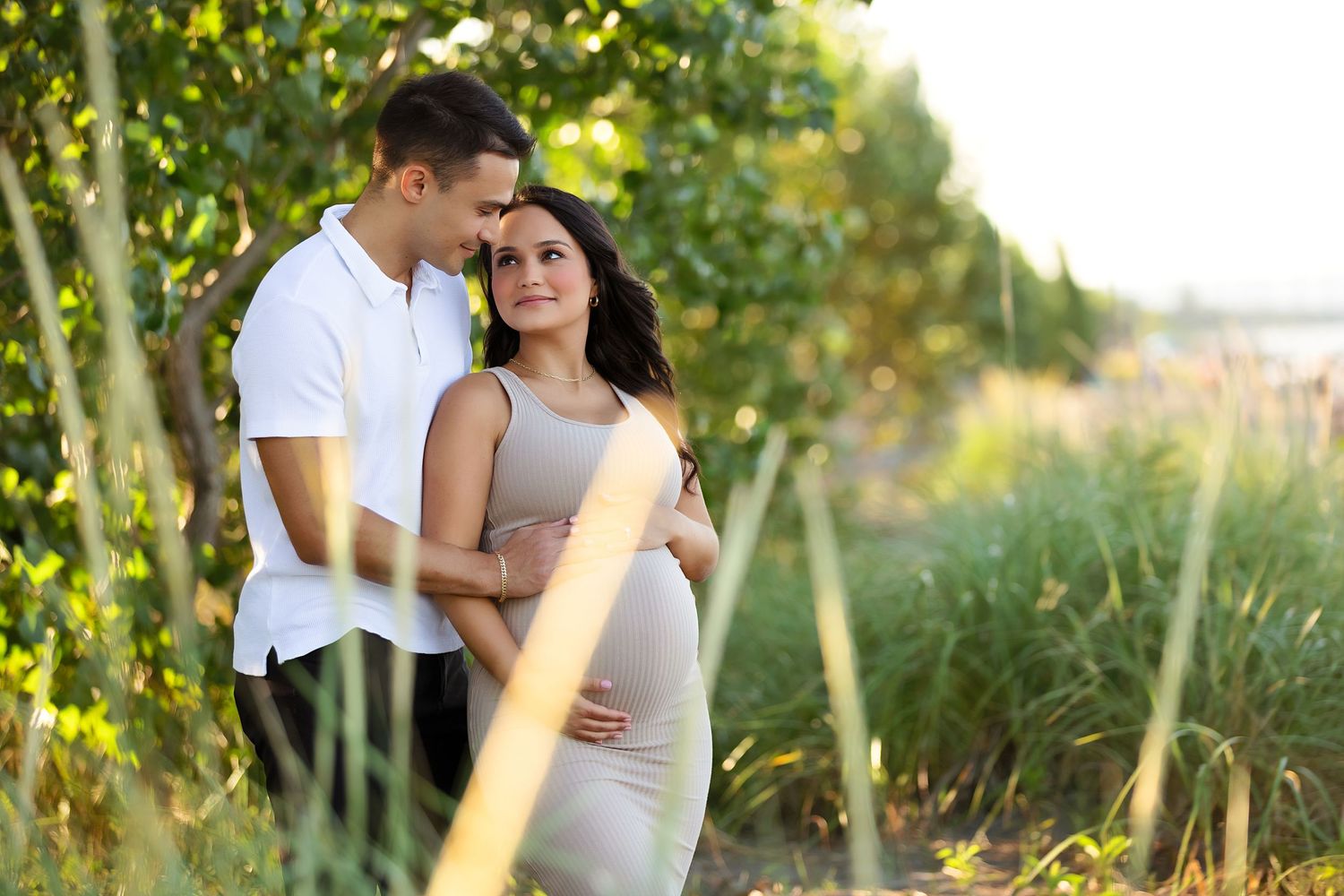 Couple embraces during sunset maternity photo session among trees.