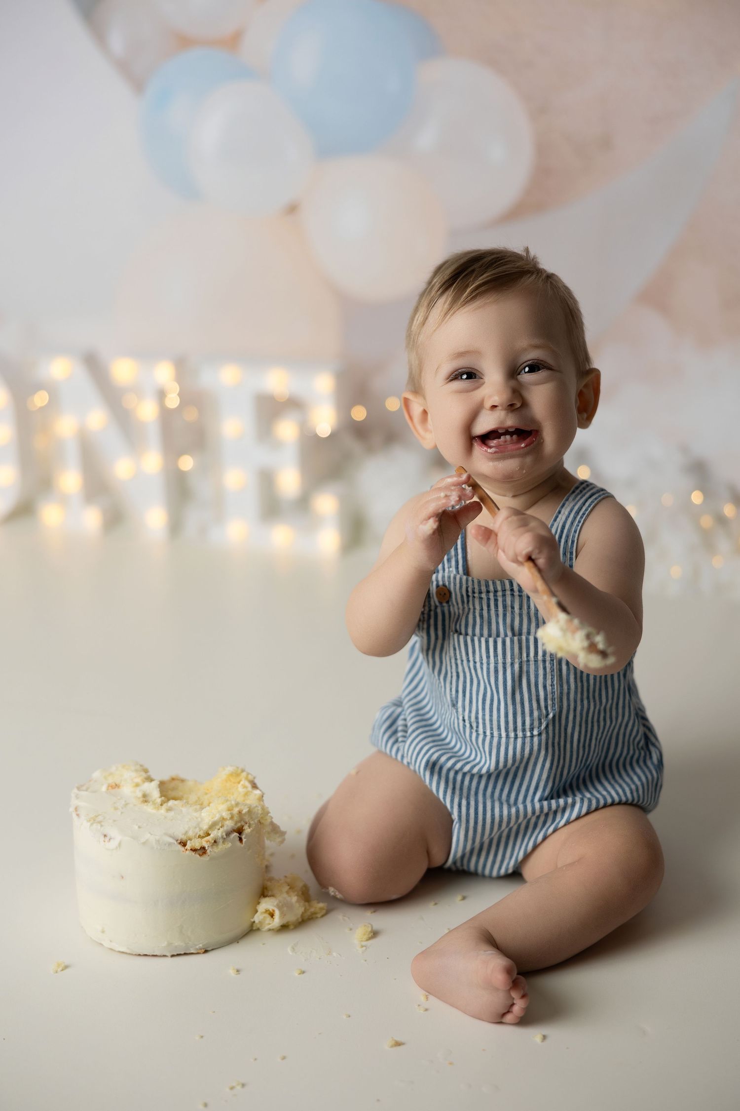 A one year cake smash photoshoot featuring a white cake and blue and white decor.