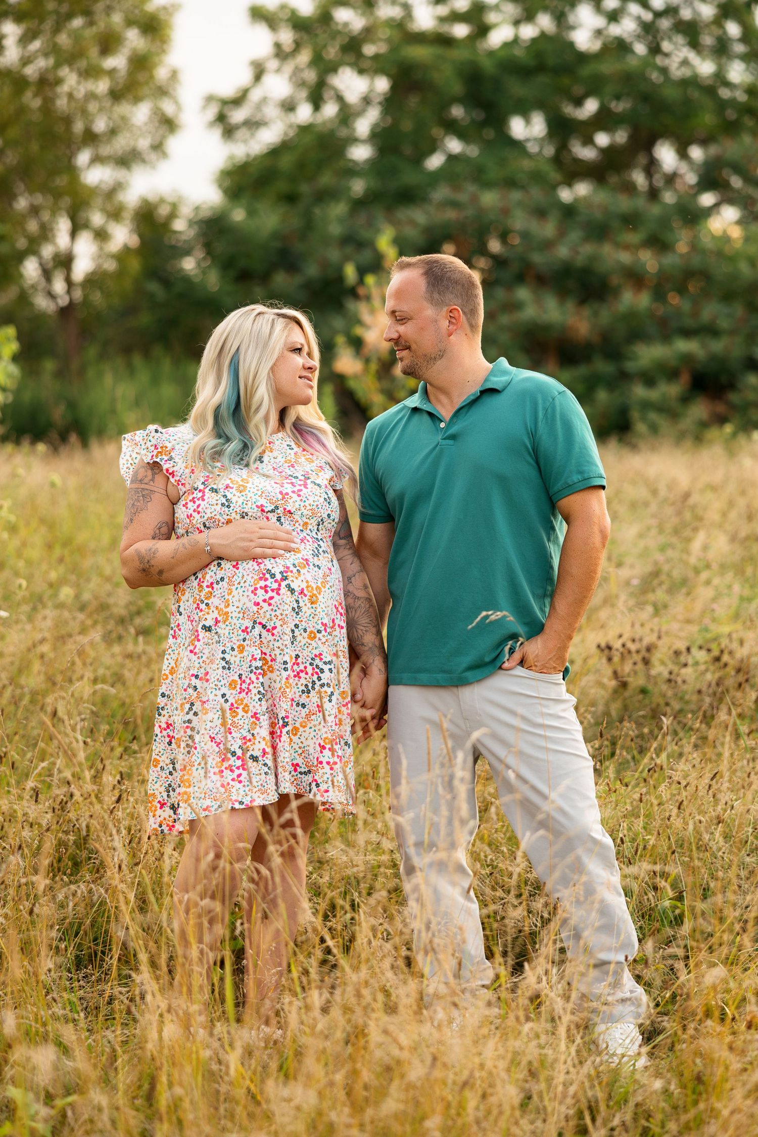 Two people embrace while standing in a golden field during sunset, creating a romantic outdoor scene.